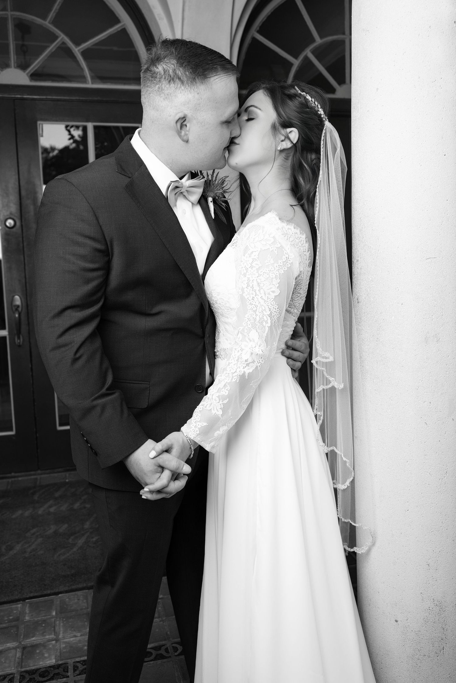 Black and white portrait of a bride and groom embracing face-to-face under an outdoor archway