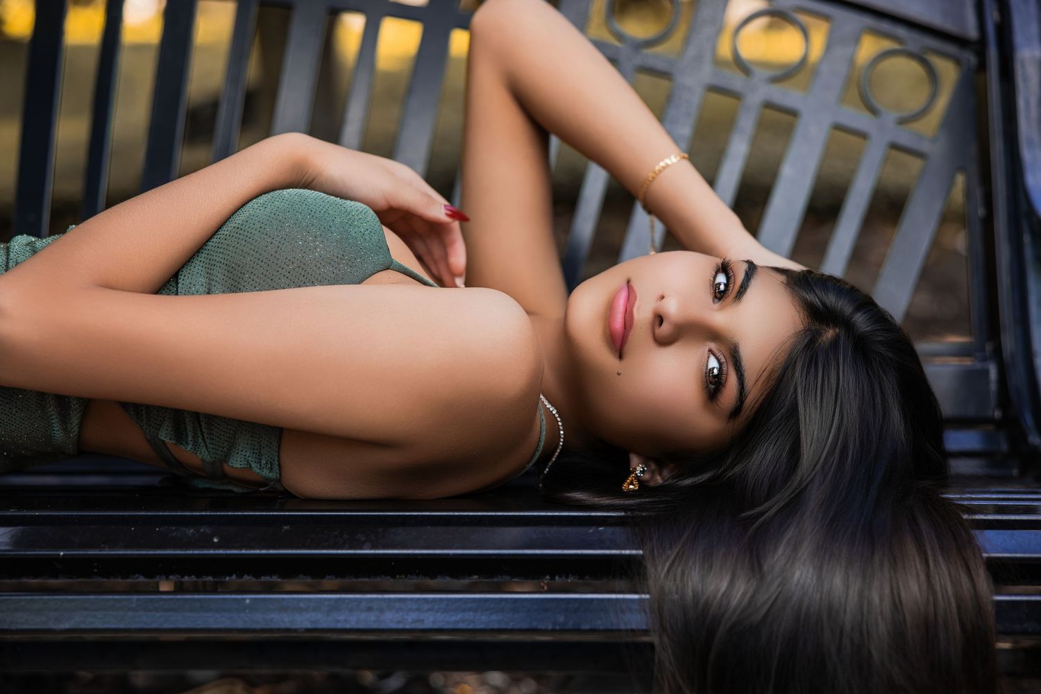 Young woman with long straight dark hair lying down and posing on an outdoor bench