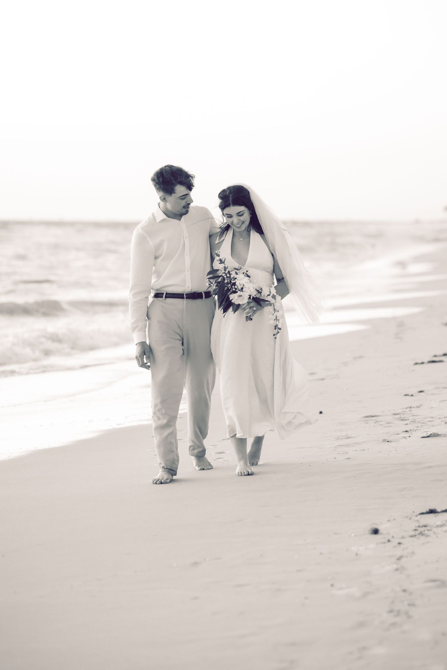 Newlywed couple walking hand-in-hand along the sandy shore during a beach wedding