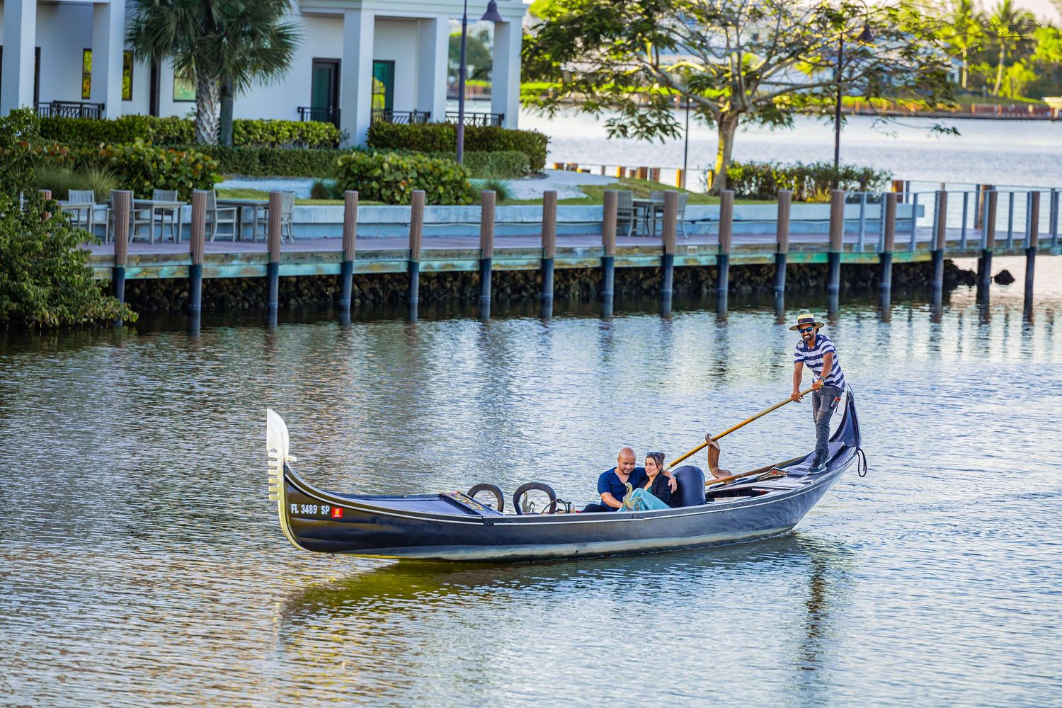 Gondolier rowing passengers down a river path in front of a wooden dock boardwalk