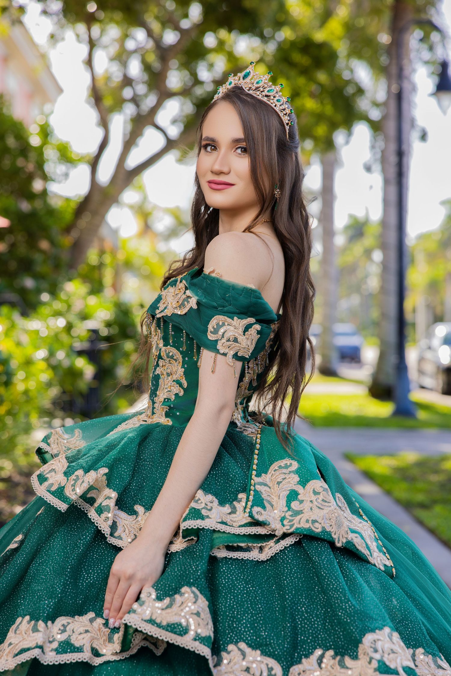 Young woman wearing a tiered emerald green ballgown with gold lace embroidery in an outdoor garden