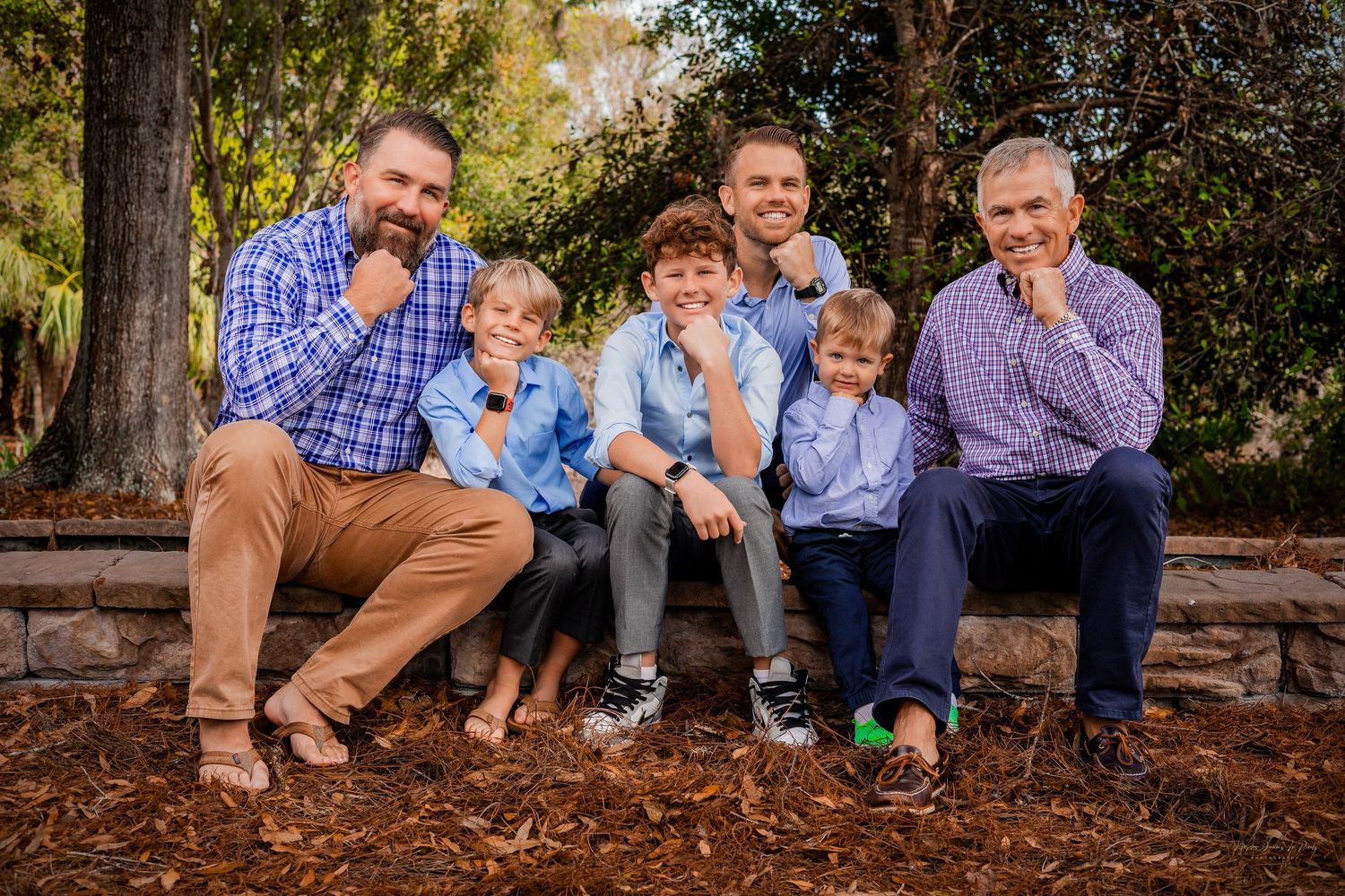 Multigenerational family portrait of five men and boys sitting together outside on a stone wall