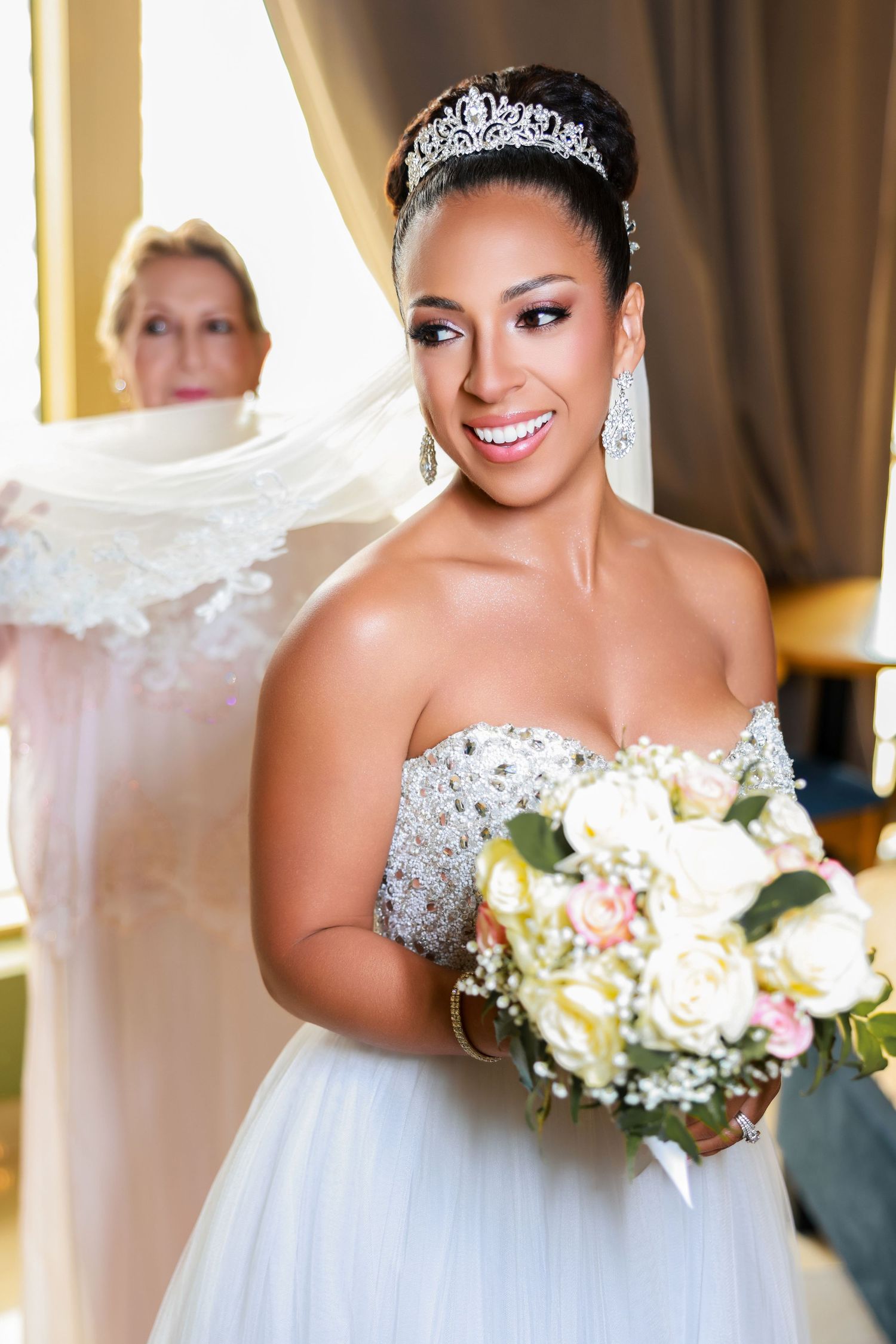 Smiling bride in a strapless embellished wedding gown holding a floral bouquet while getting ready