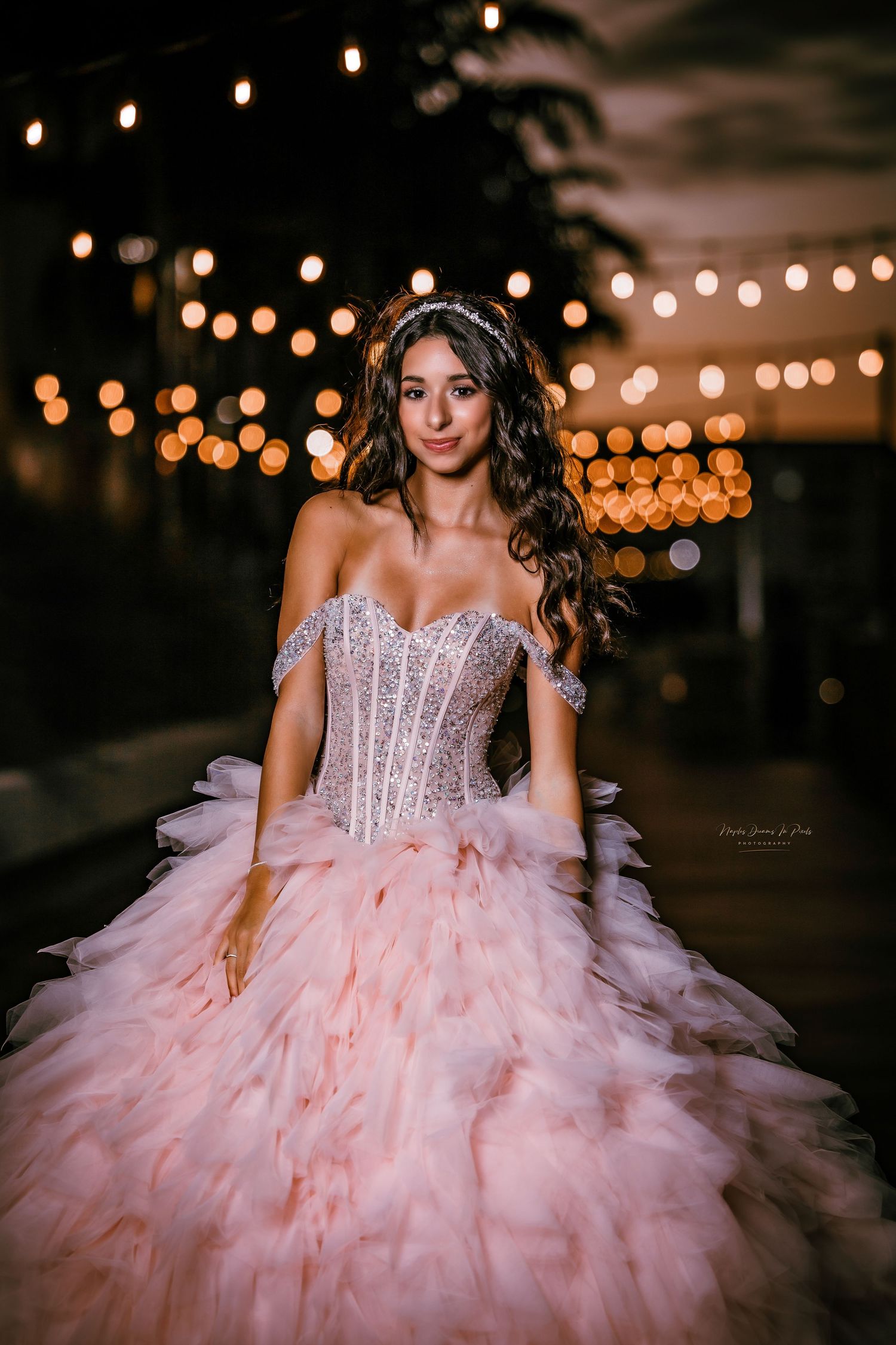 Glamour portrait of a woman in an embellished pink ruffled ballgown under outdoor string lights