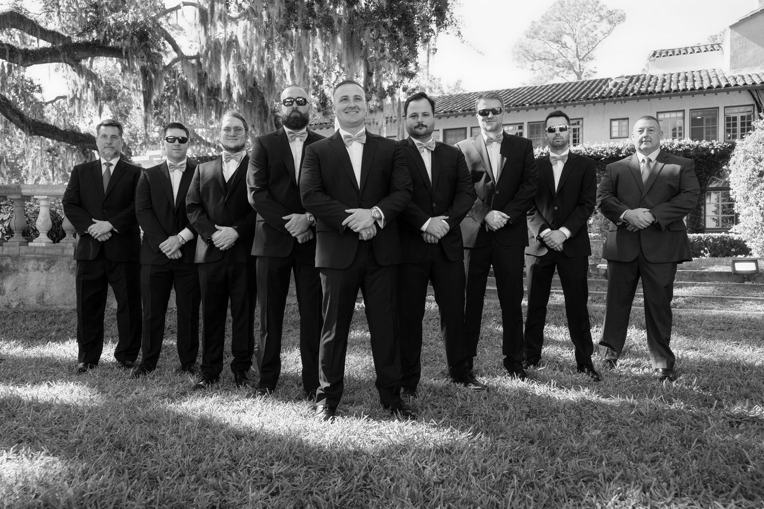 Black and white outdoor portrait of a groom standing in front of his groomsmen on a grassy lawn