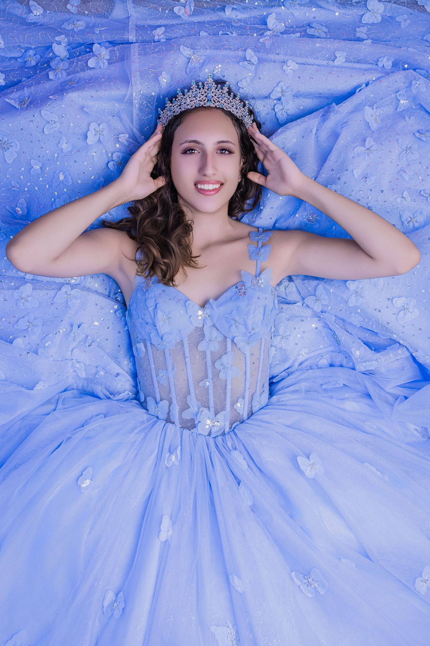 Young woman wearing a vibrant royal blue ballgown and a matching tiara posing against a textured background