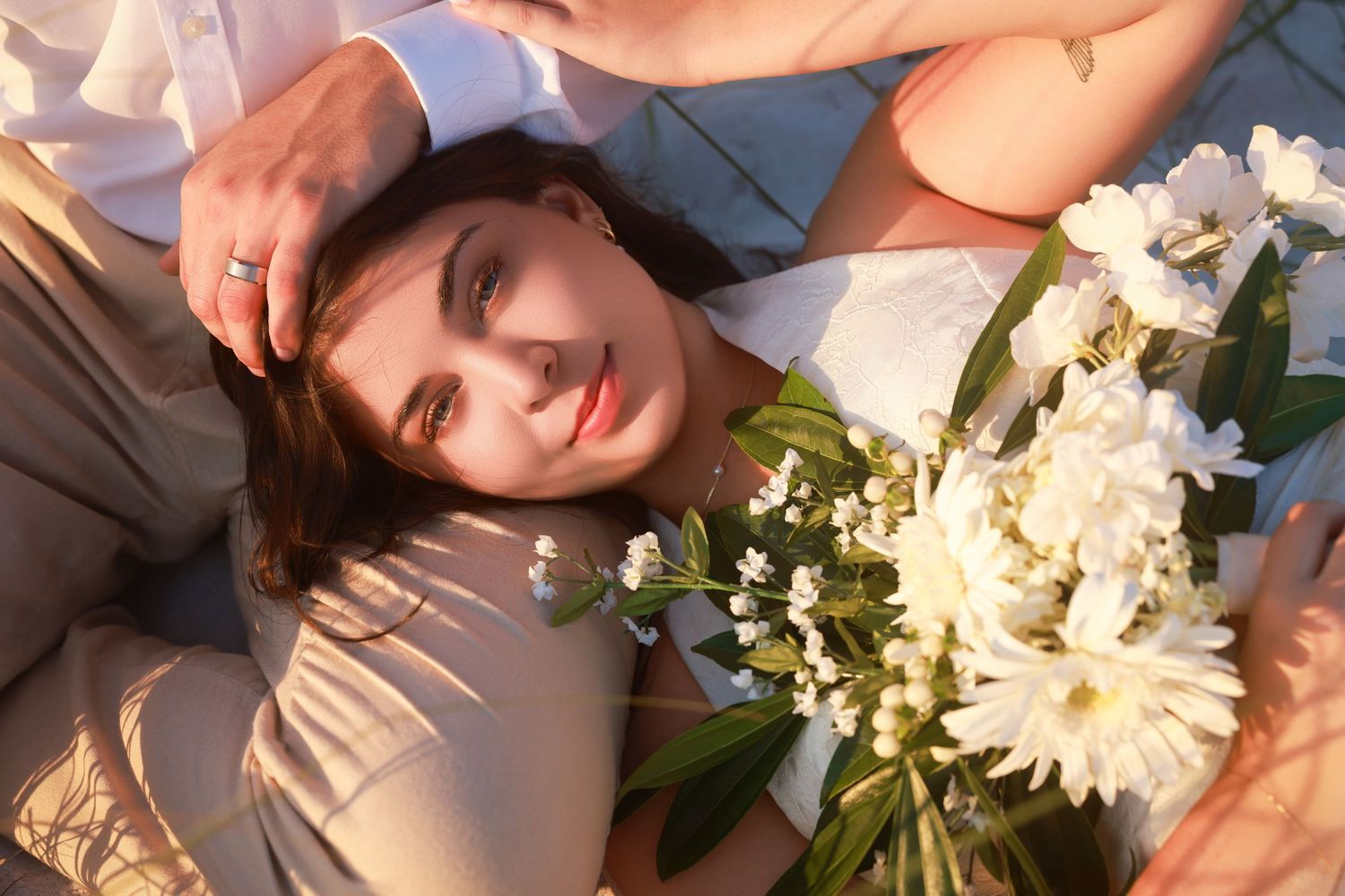 Close-up overhead view of a woman holding a white floral bouquet while resting in her partner's lap