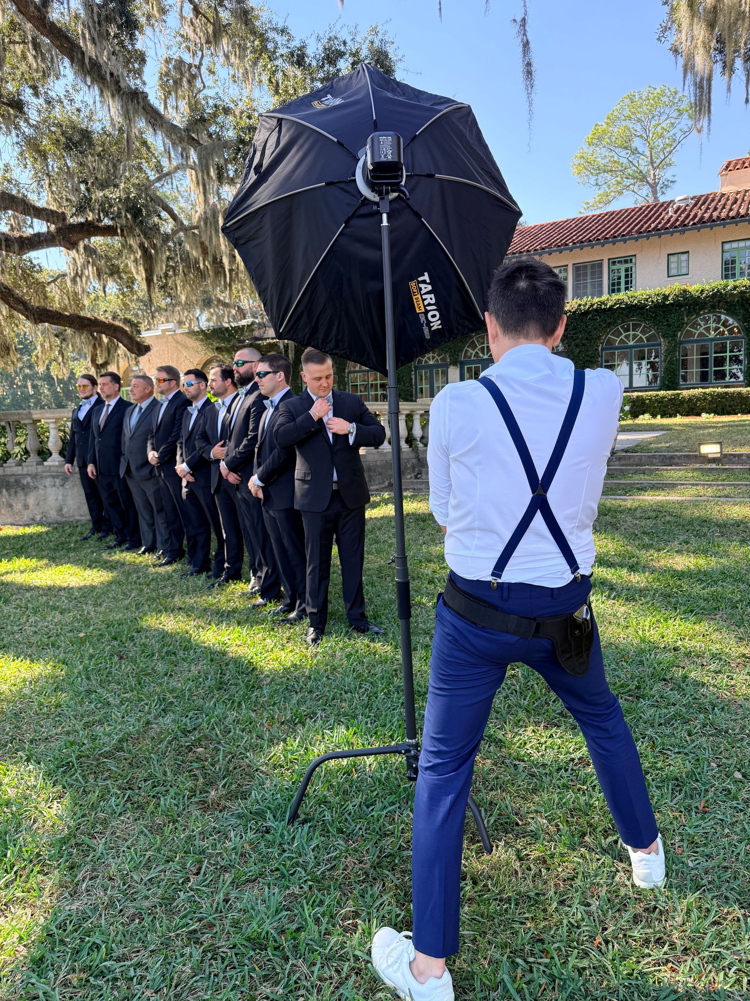 Behind-the-scenes wedding photo showing the photographer photographing groomsmen in a line outside.