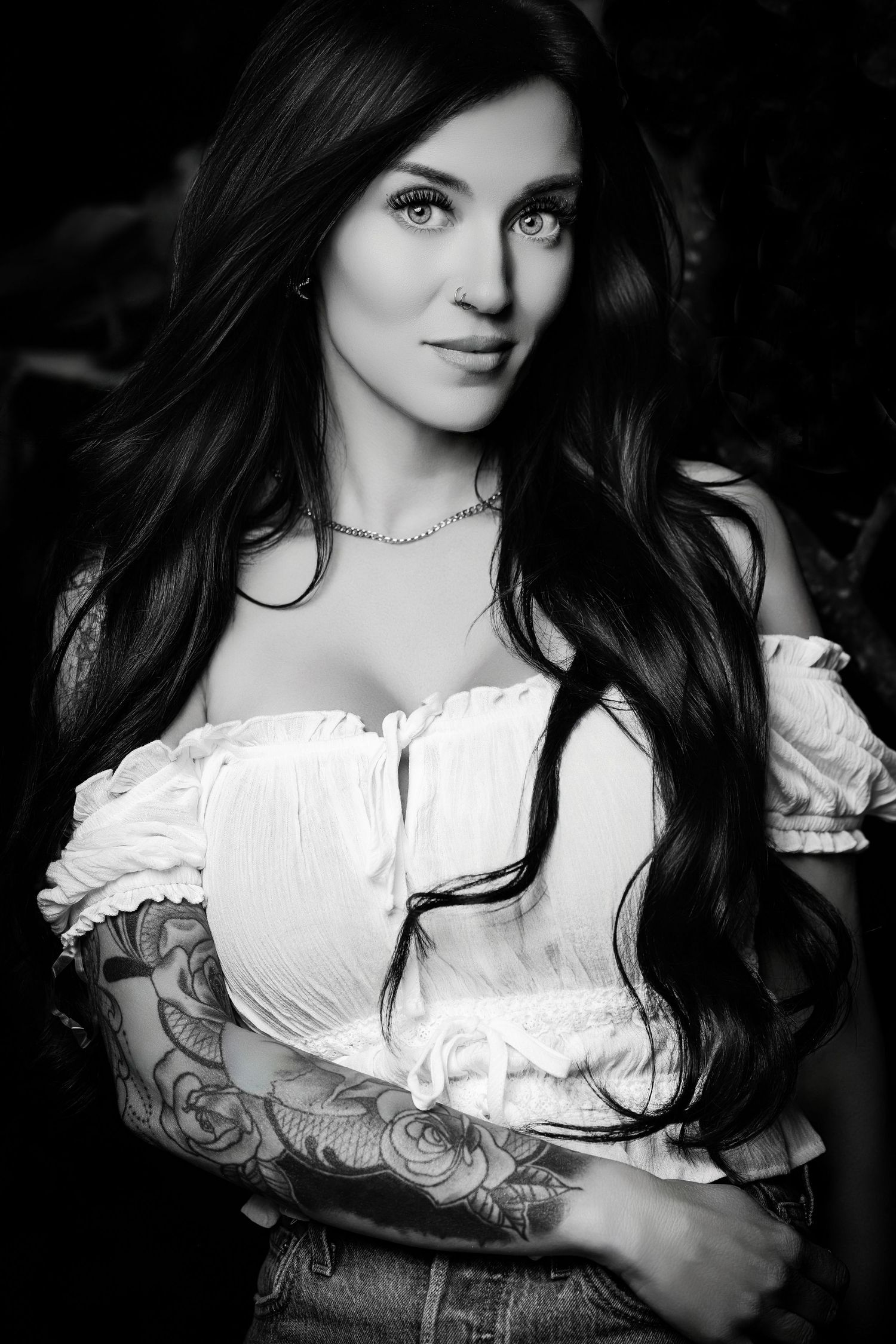 Black and white portrait of a woman with long wavy dark hair and shoulder tattoos