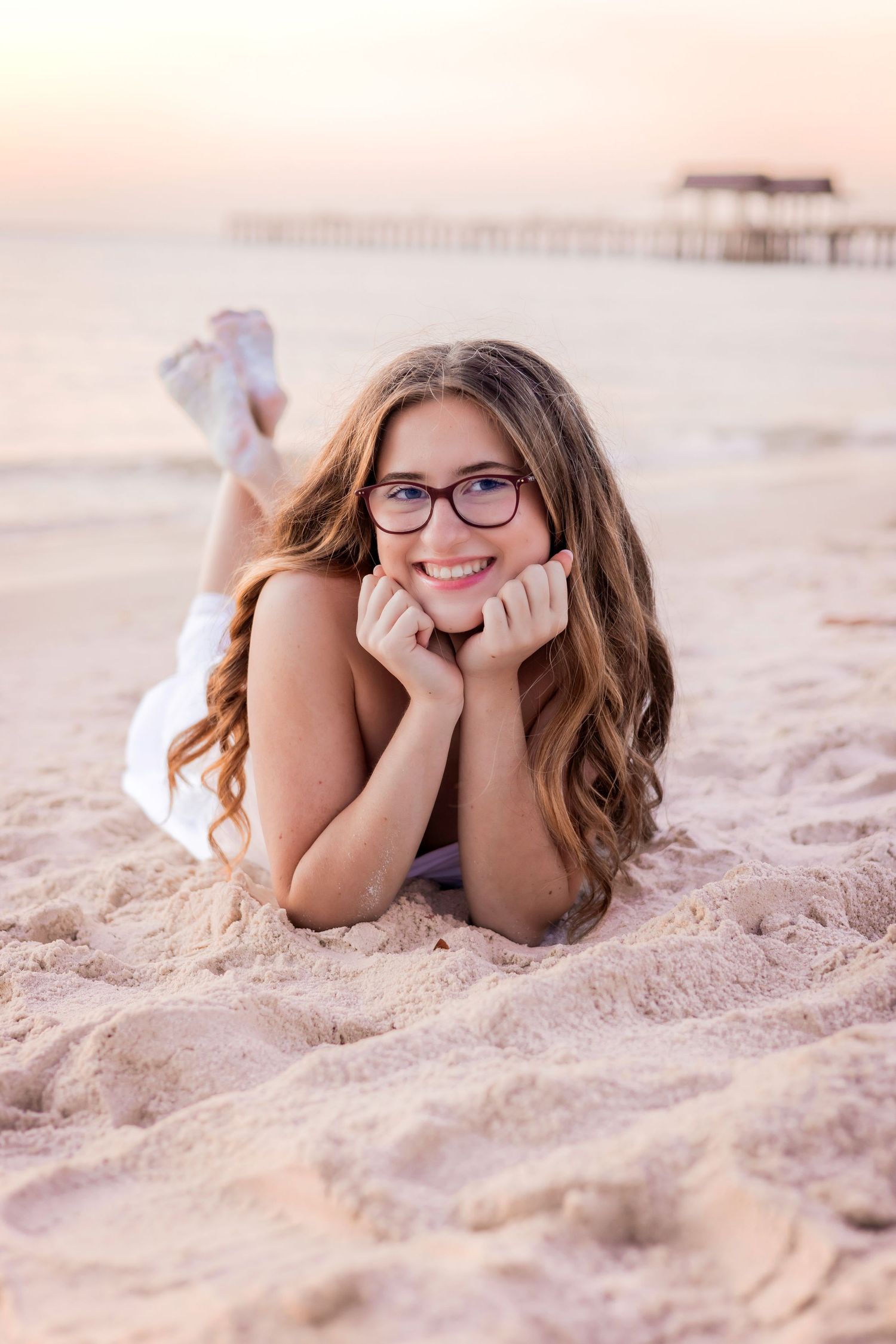 Smiling teenage girl lying on her stomach on a sandy beach shore during sunset