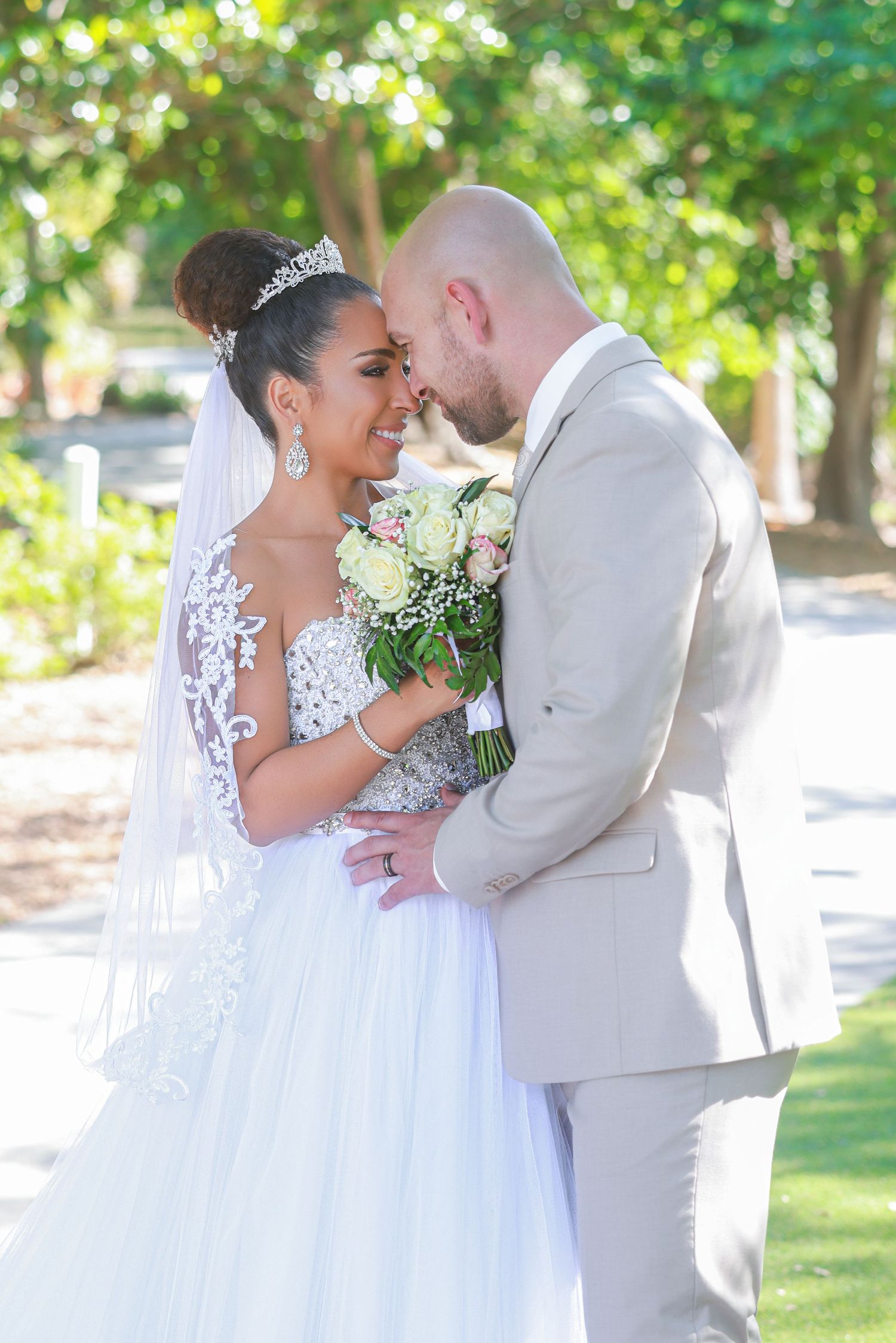 Newlywed bride and groom smiling face-to-face in a sunny outdoor garden setting.
