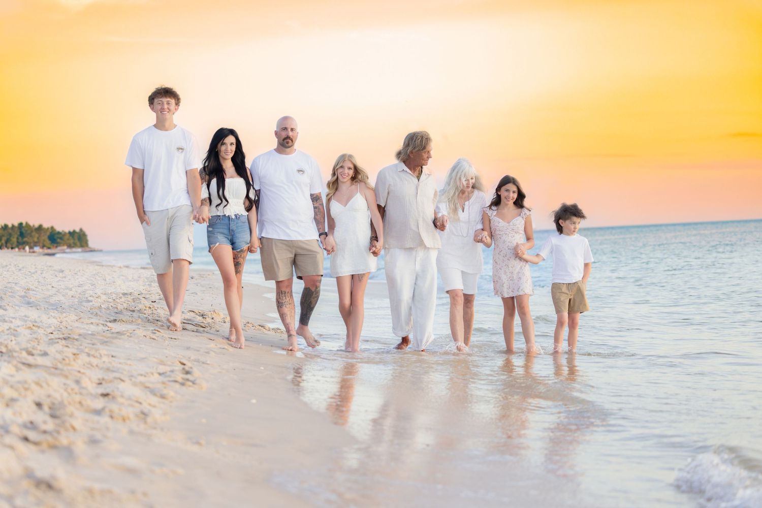 Large family walking barefoot along the ocean shoreline during a beach vacation at sunset.