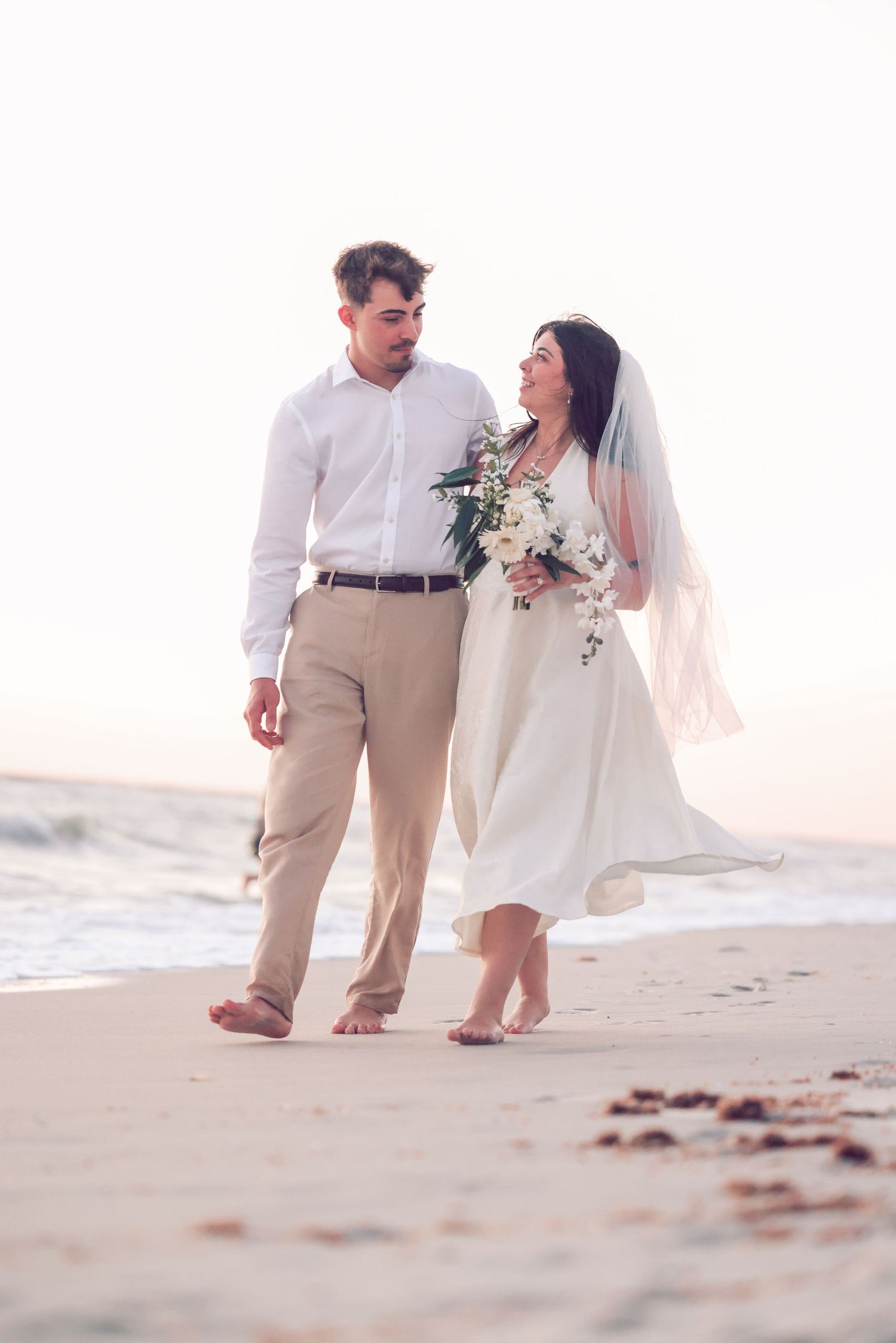 Bride and groom standing together on a sandy beach shore during a golden sunset wedding