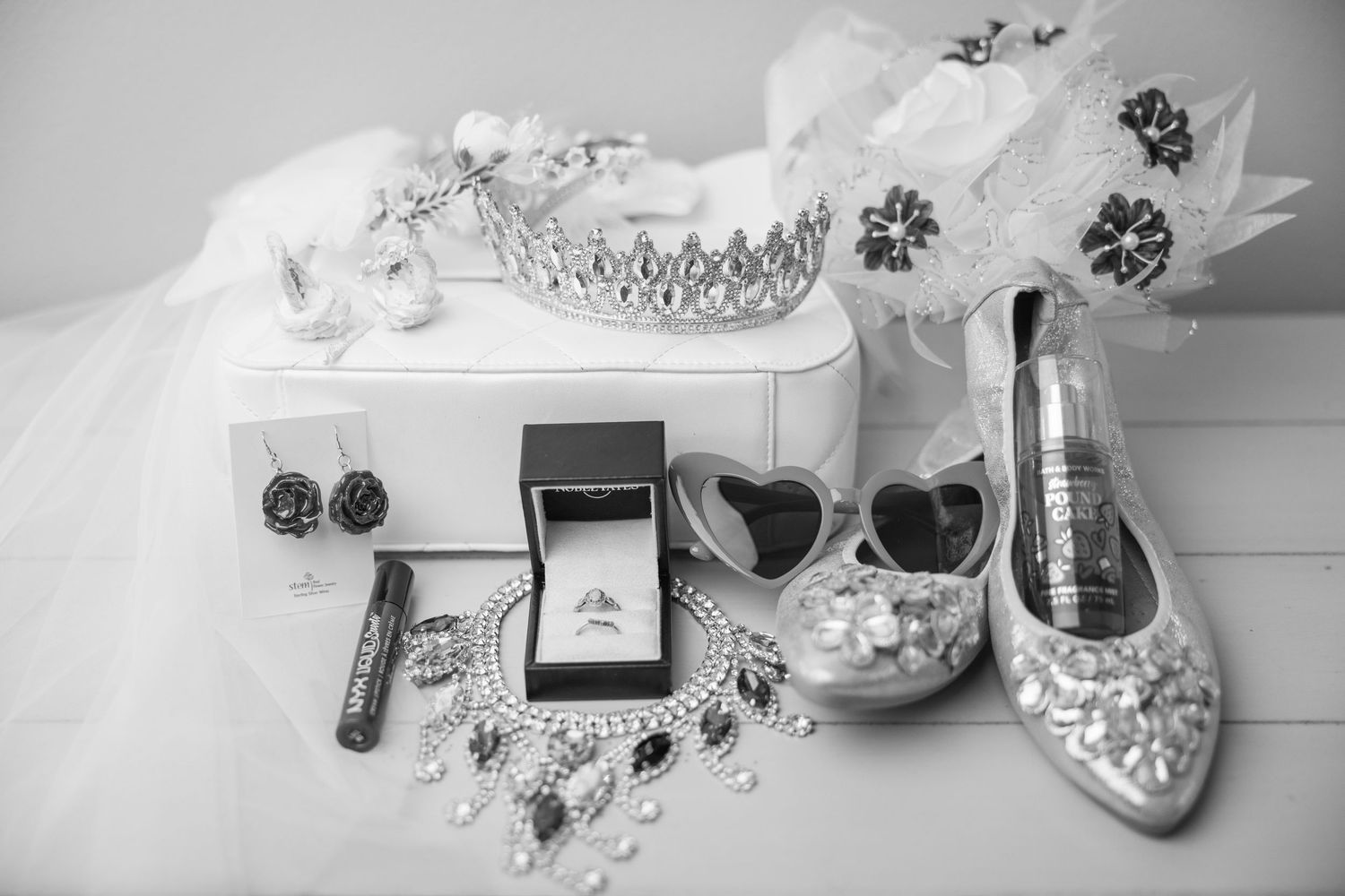 Black and white flat lay arrangement featuring an engagement ring, tiara, jewelry, and sparkly wedding high heels