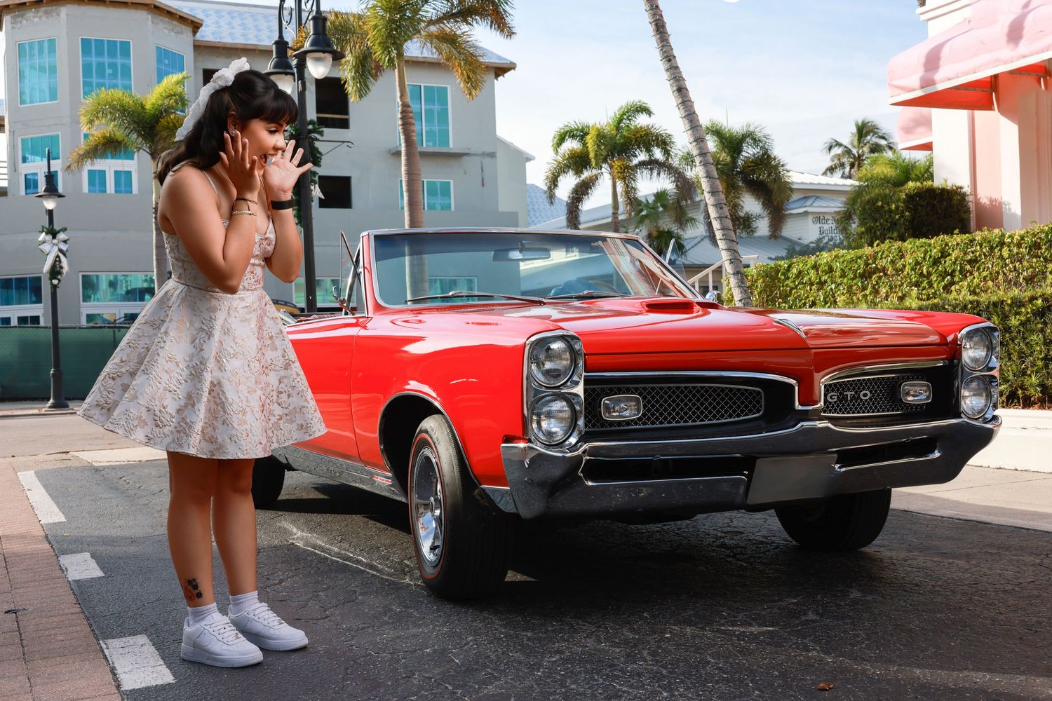 Surprised young woman in a short dress posing next to a classic red convertible car outdoors