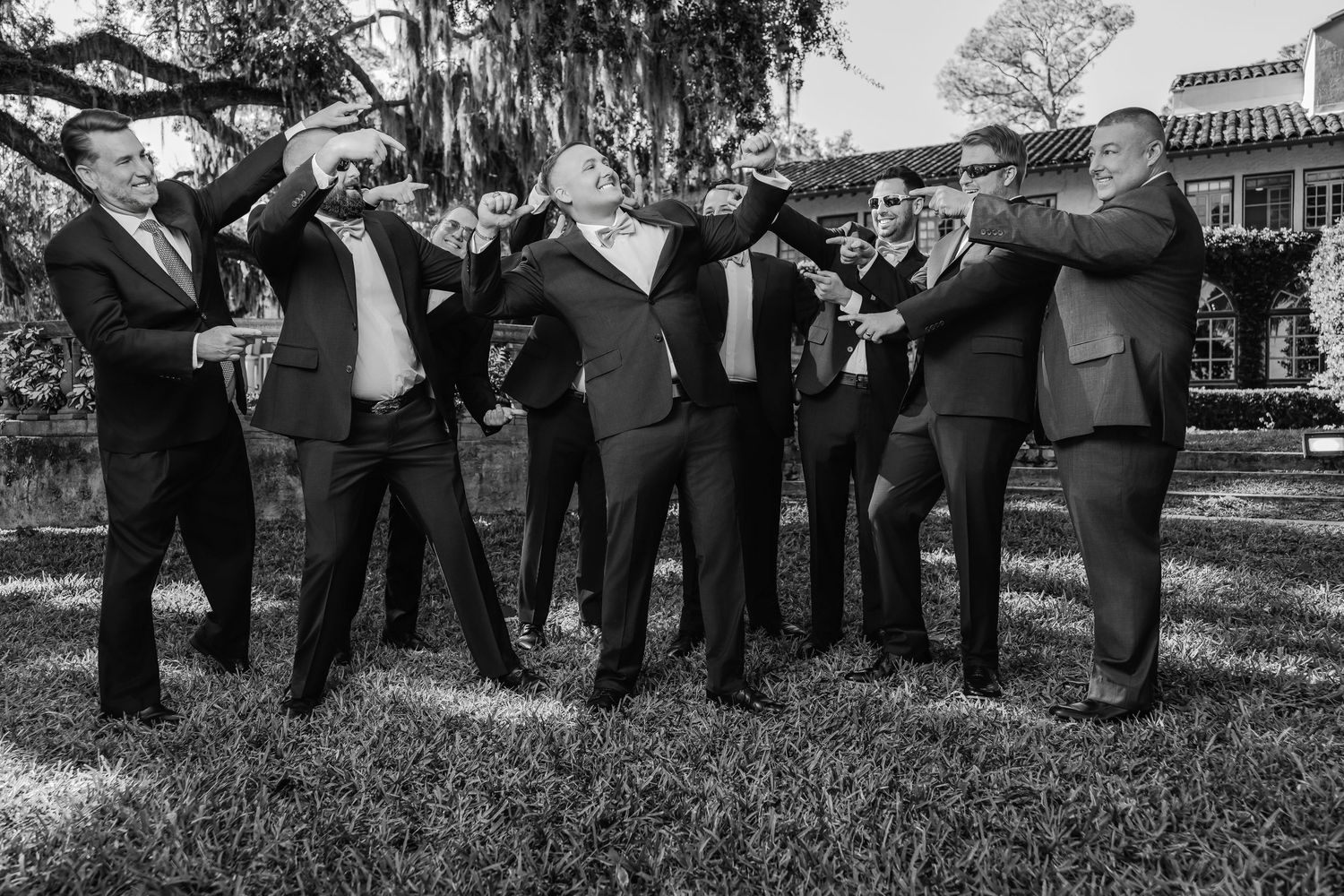 Black and white outdoor portrait of groomsmen in suits striking a synchronized pose on a grassy lawn