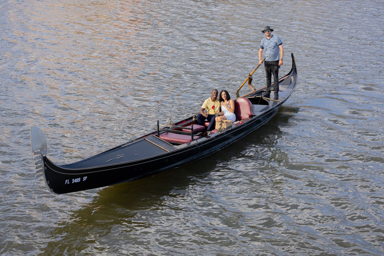 High-angle view of a gondolier navigating a traditional black gondola boat with passengers on a river.