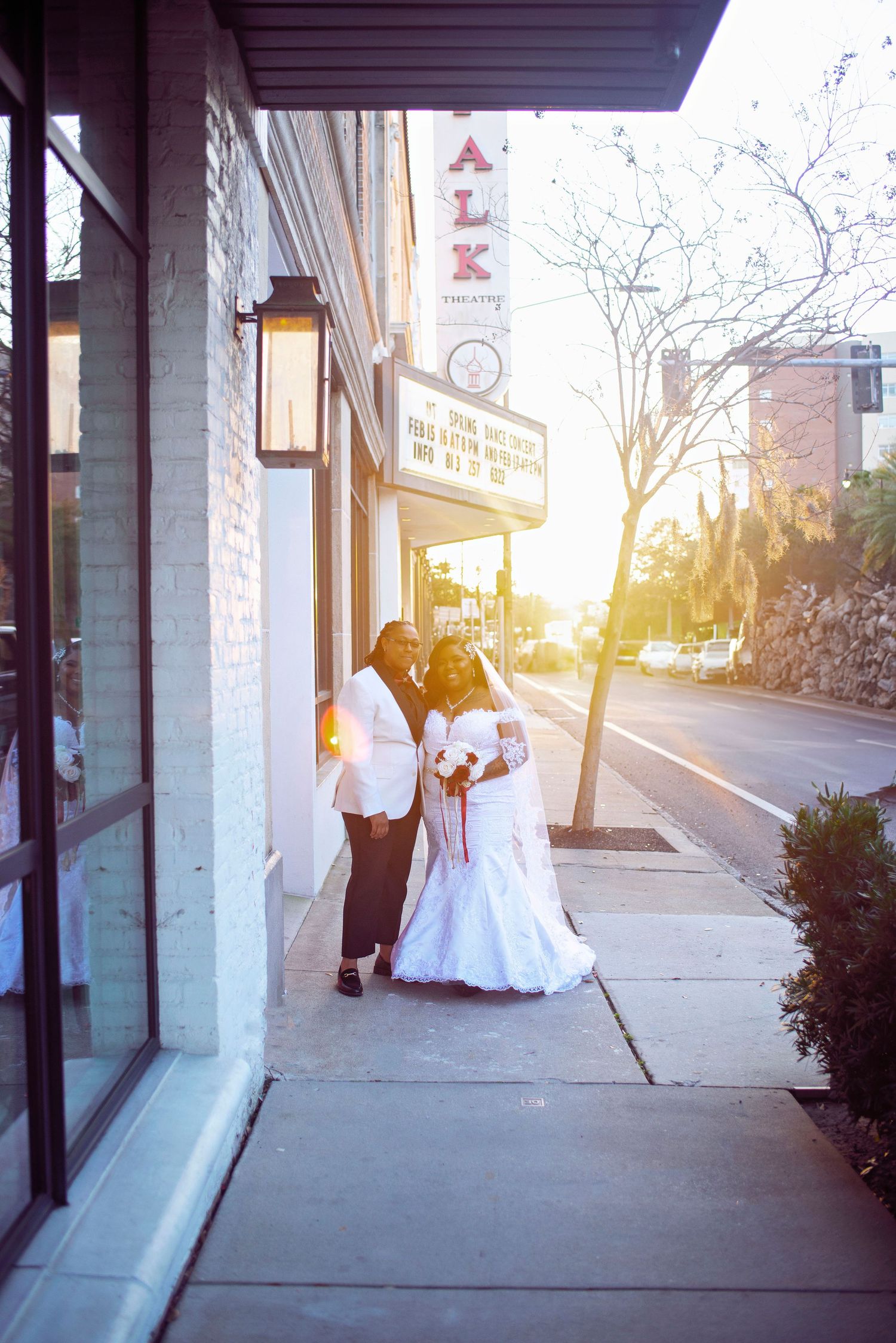 Wedding couple poses on urban sidewalk at sunset outside ALK venue with warm golden light.
