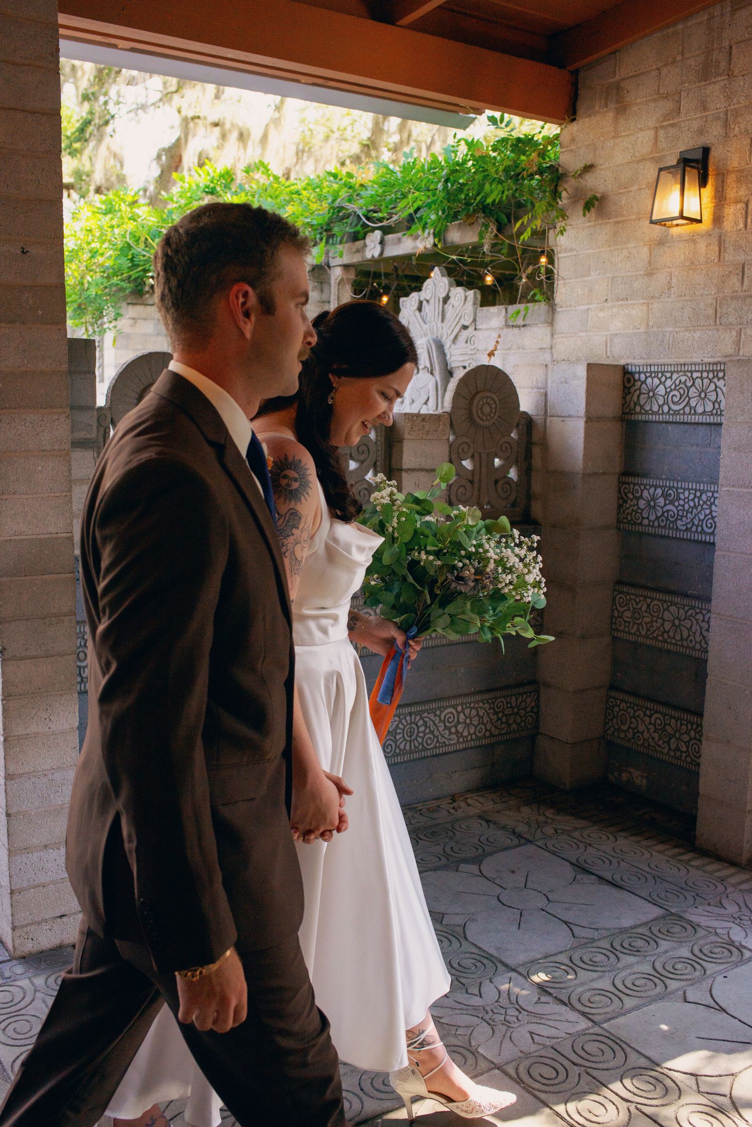 A bride holding a green bouquet and groom in a dark suit walk hand in hand at their wedding.