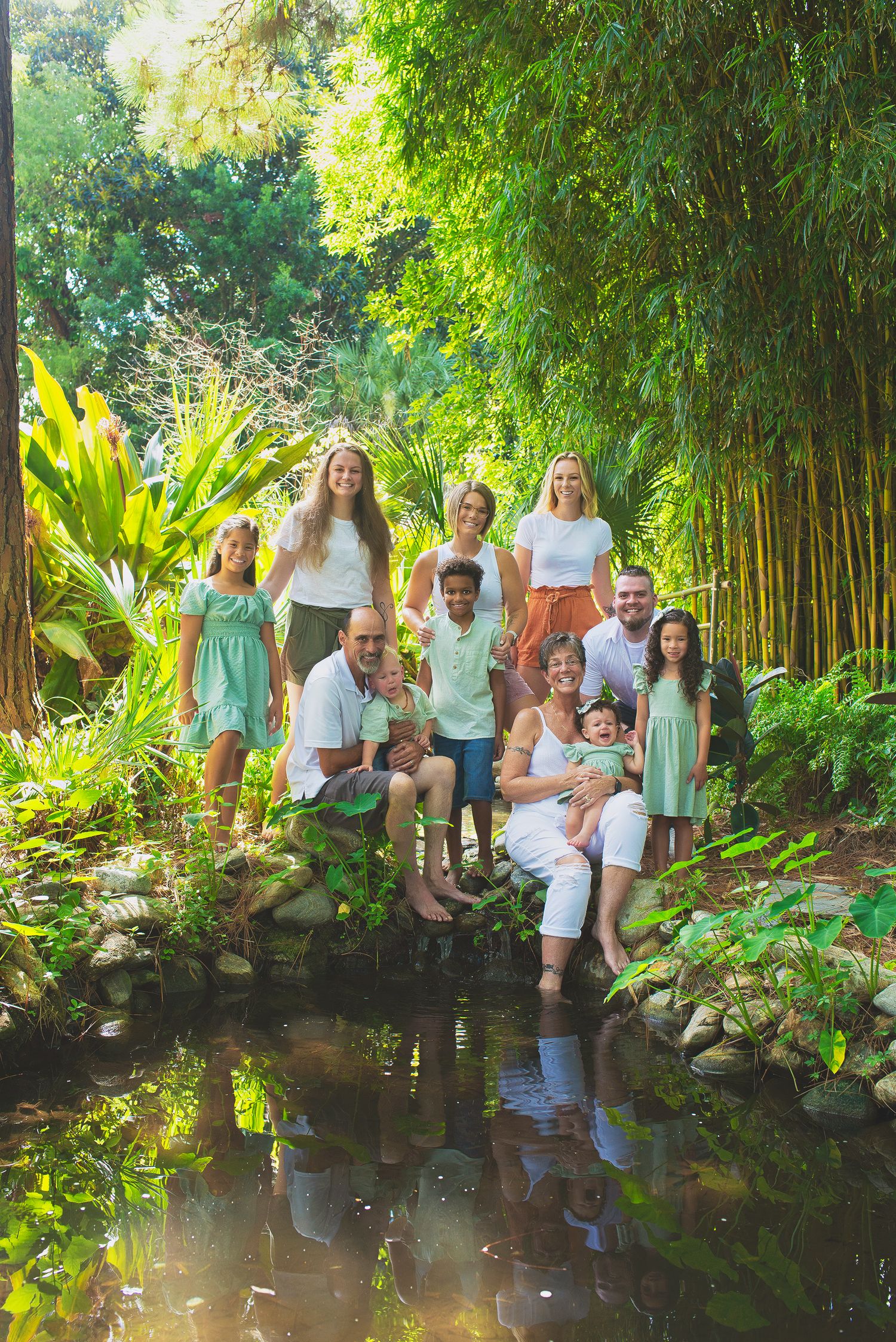 Large multigenerational family posing together beside a pond surrounded by tropical bamboo garden.