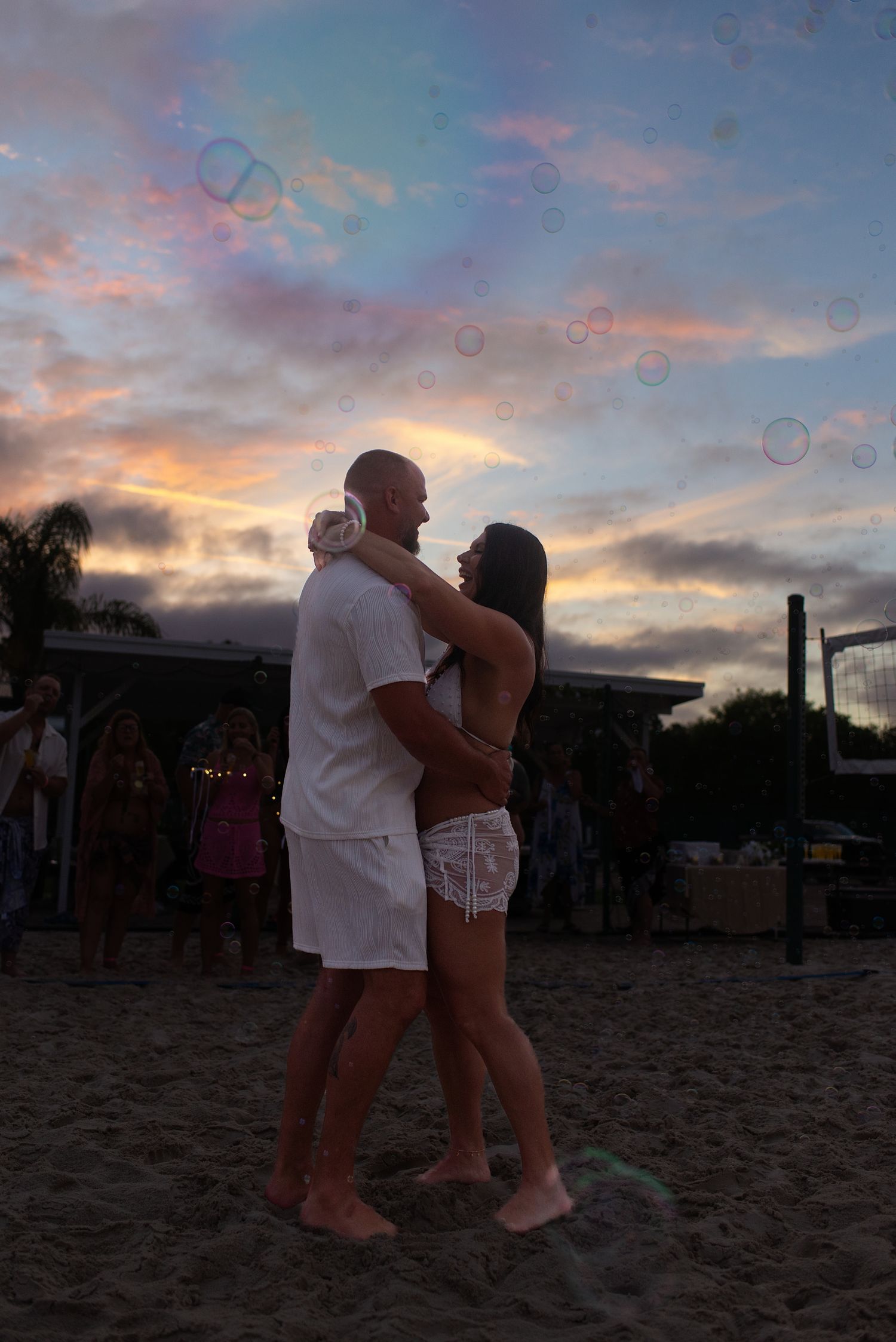 Couple dancing in silhouette on beach at sunset surrounded by floating soap bubbles.