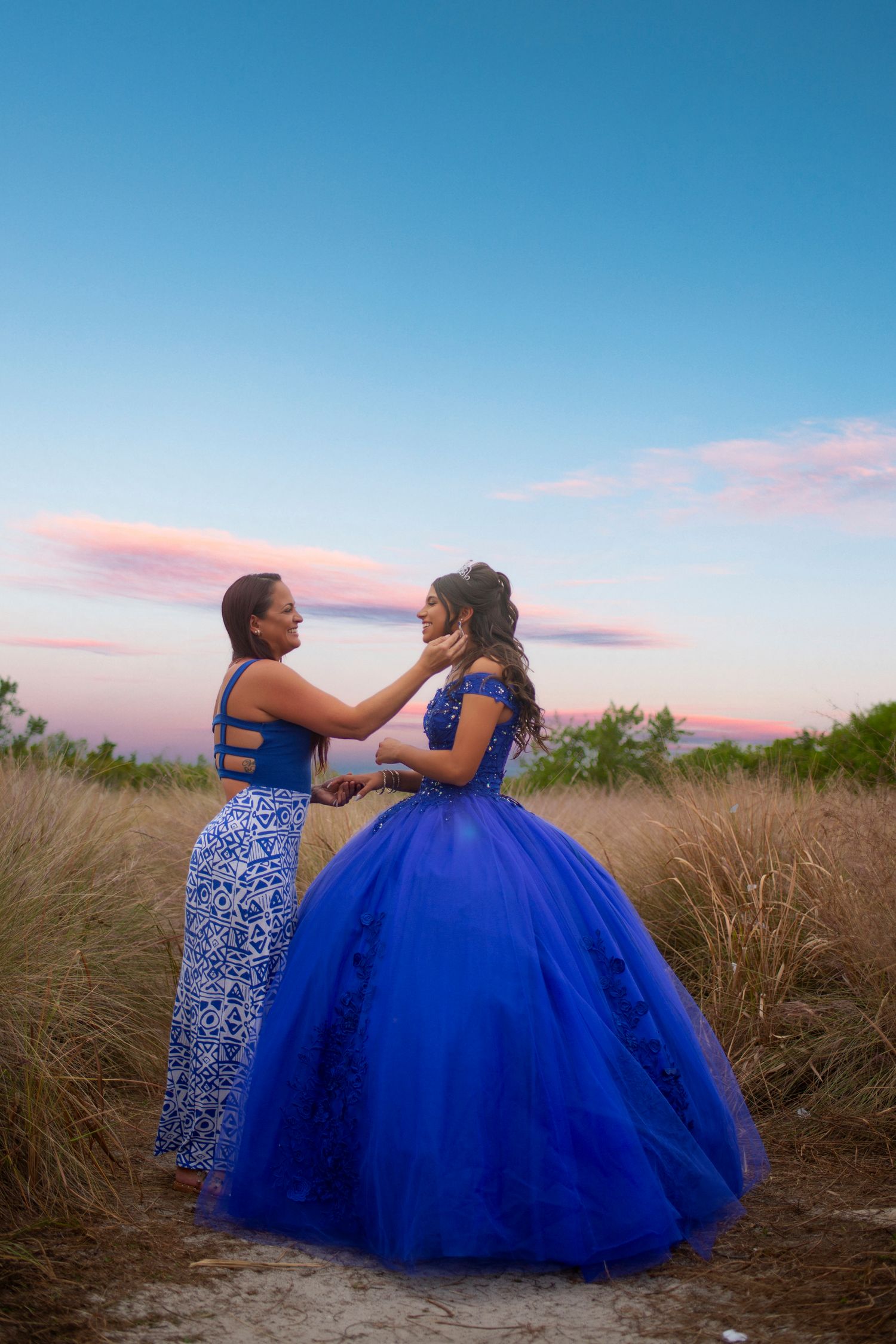 Two women in royal blue dresses pose in a golden field at sunset.