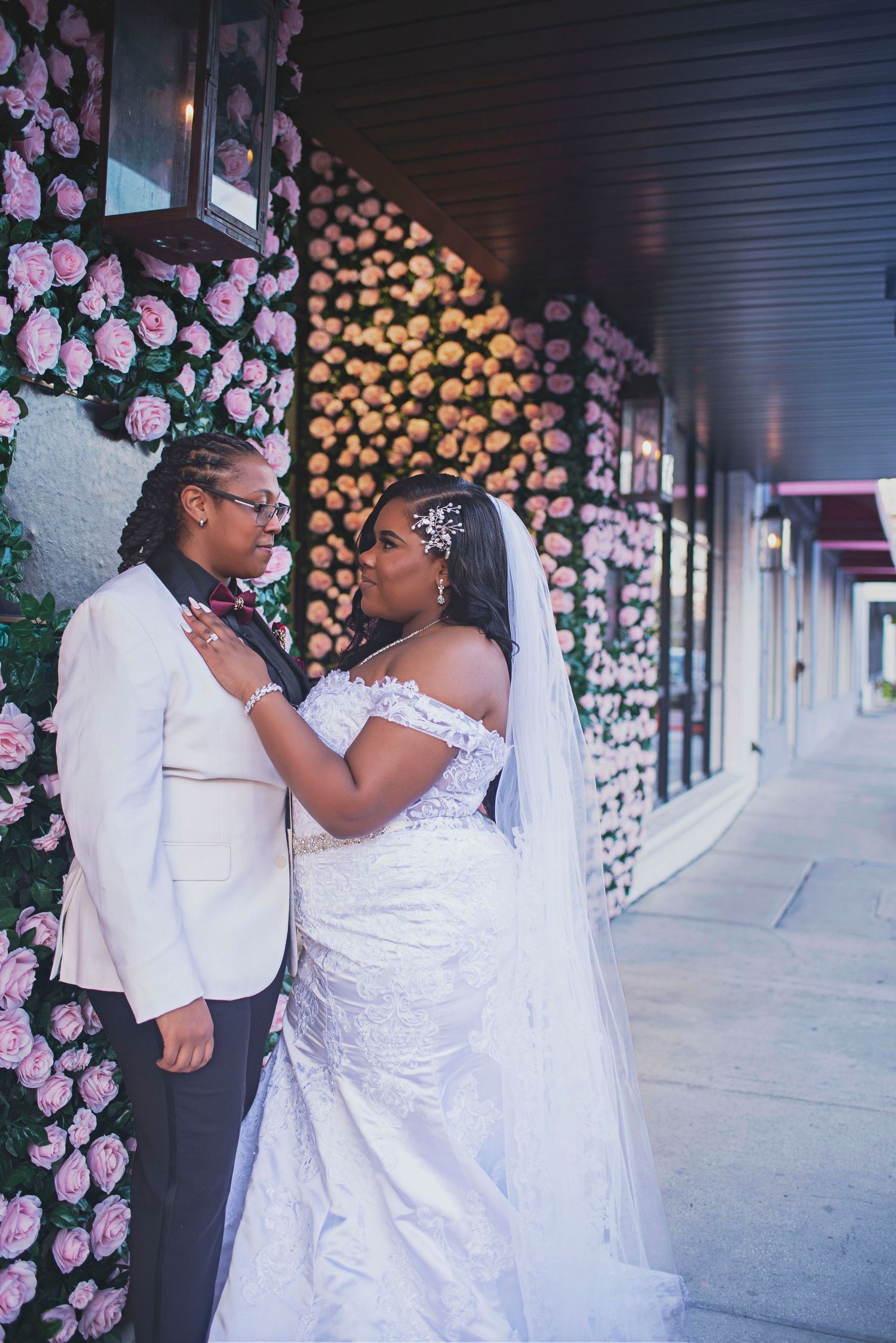 Bride and partner share an intimate moment in front of a beautiful pink floral rose wall.
