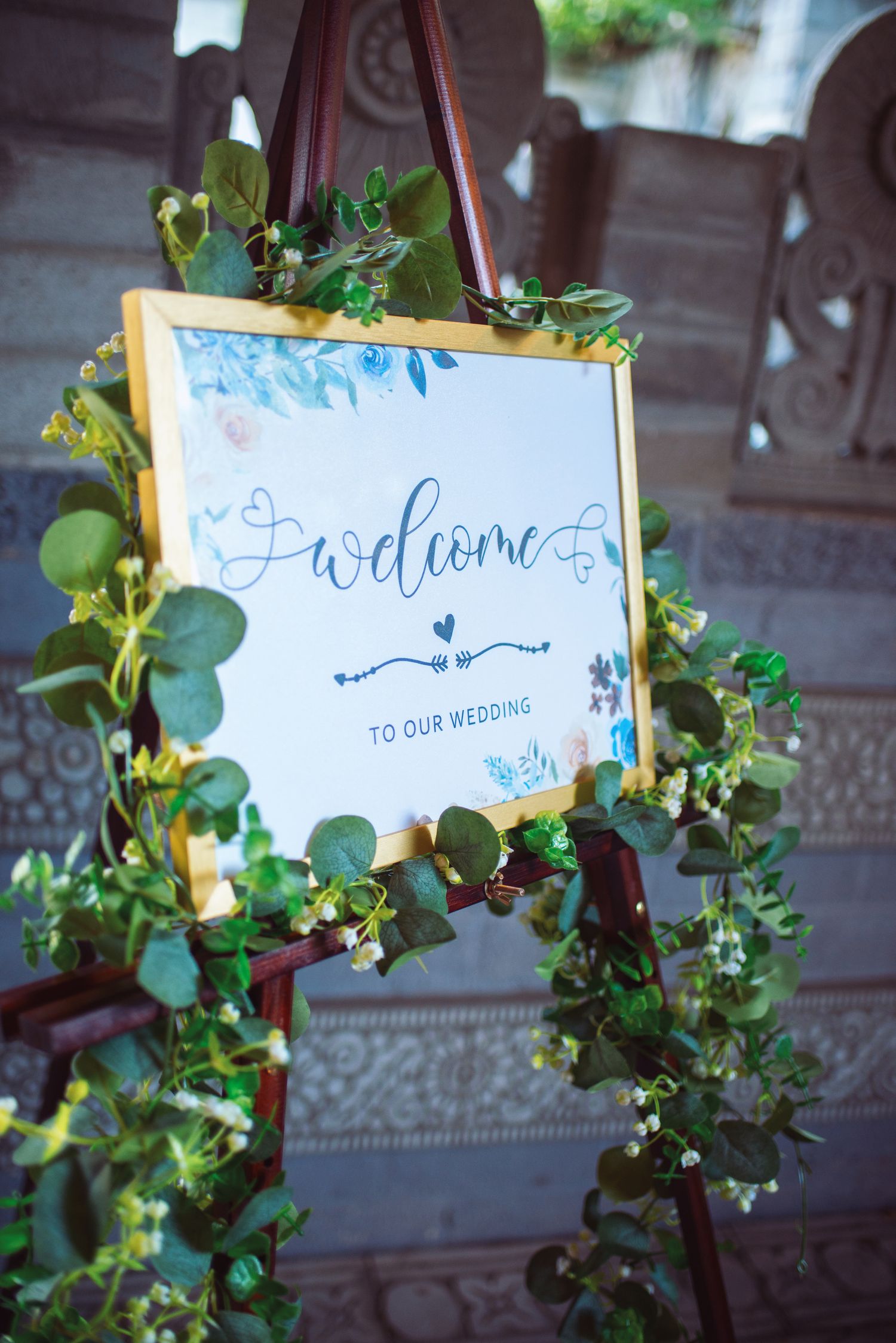 Elegant gold-framed wedding welcome sign adorned with eucalyptus greenery hangs at a venue entrance.