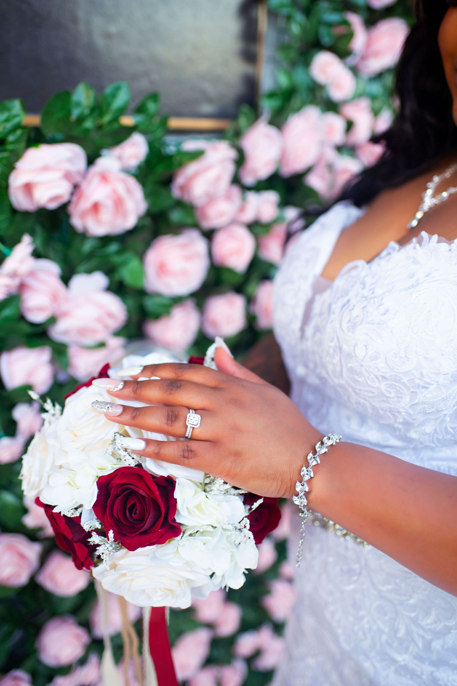 Close-up of bride's hands holding red and white rose bouquet with diamond ring and bracelet.