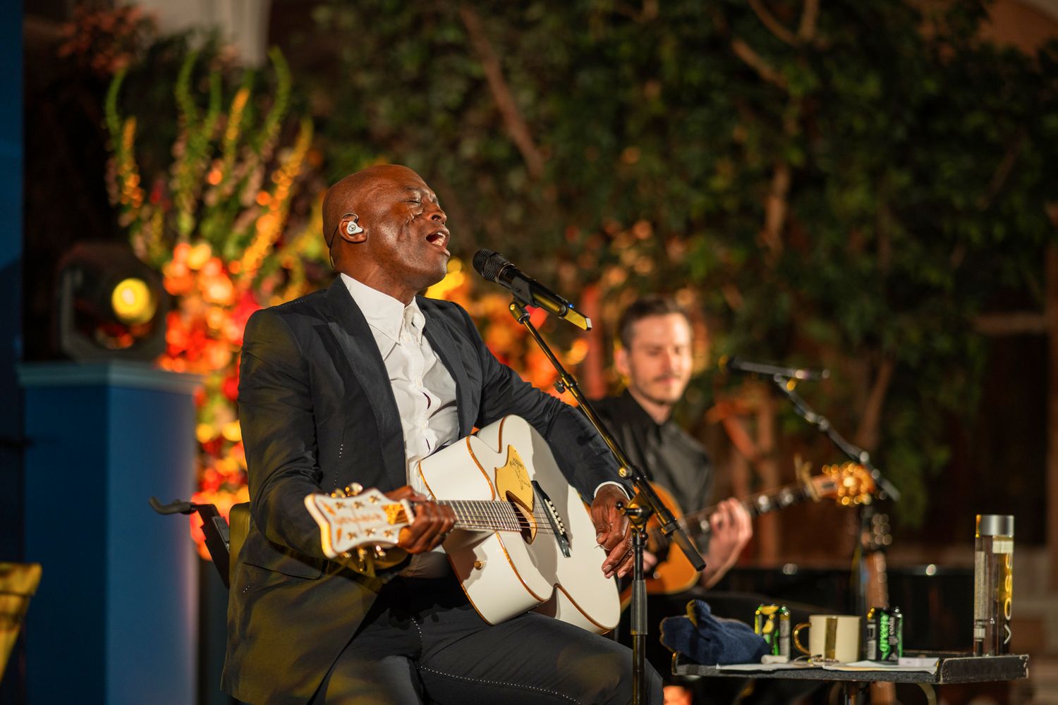 Musicians perform an acoustic set on outdoor stage with guitars at evening event.