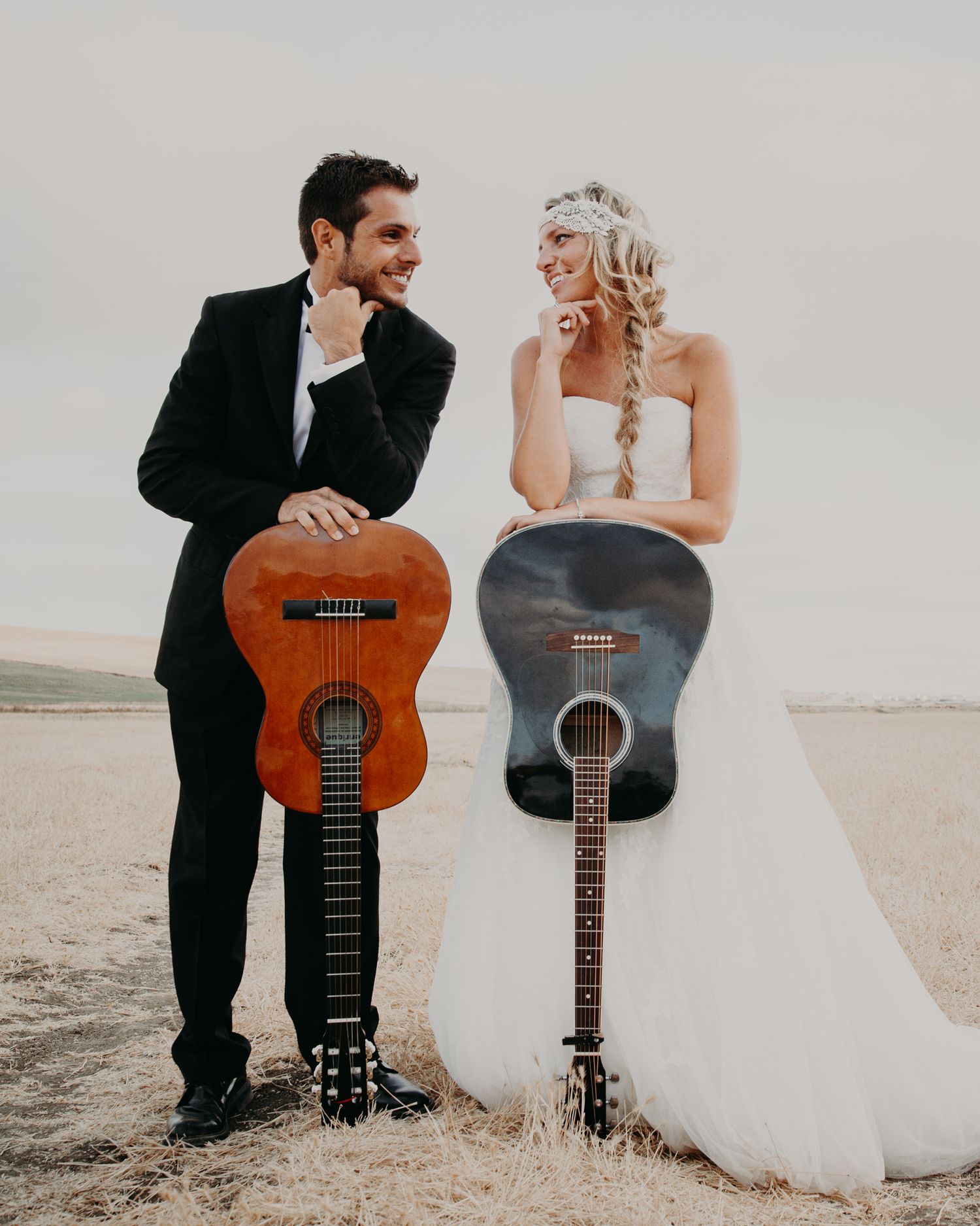 A wedding couple poses with acoustic guitars against a neutral background.