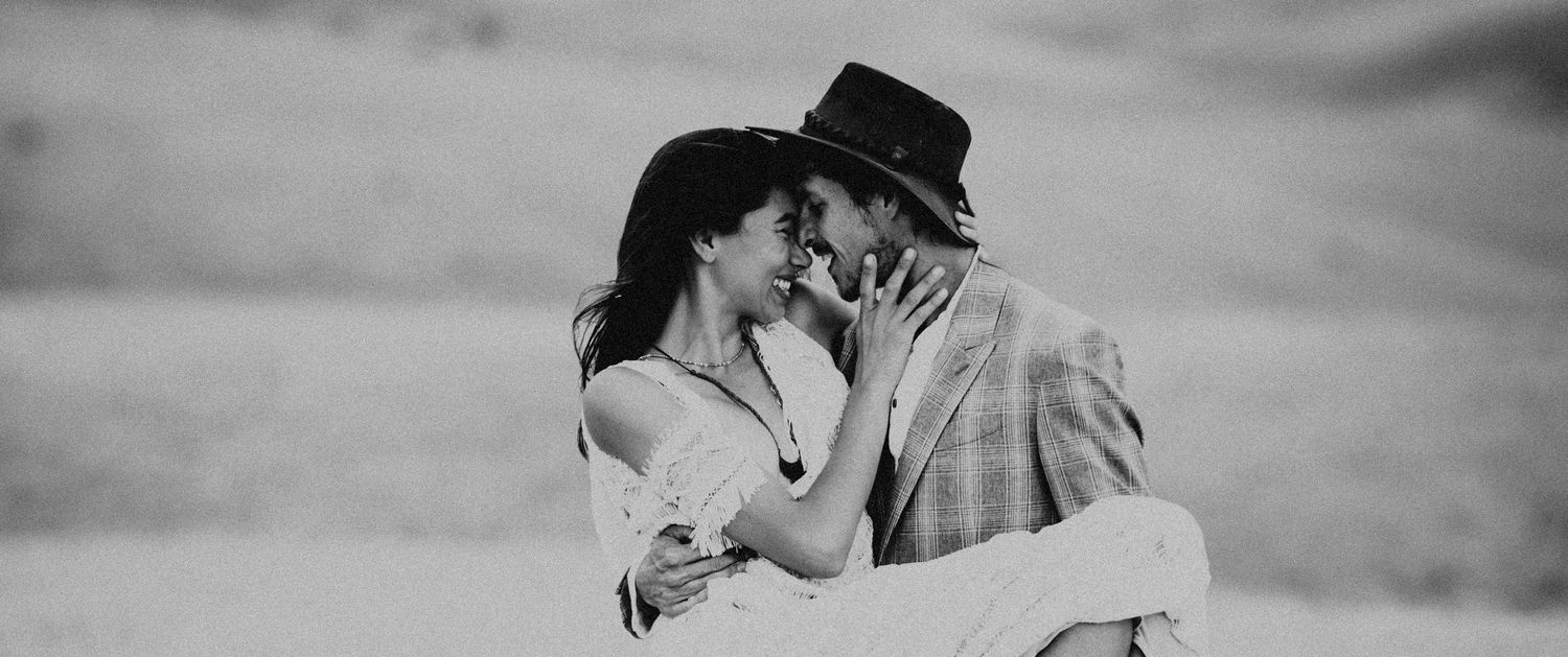 A romantic black and white photo of a couple in western attire embracing in an outdoor setting.
