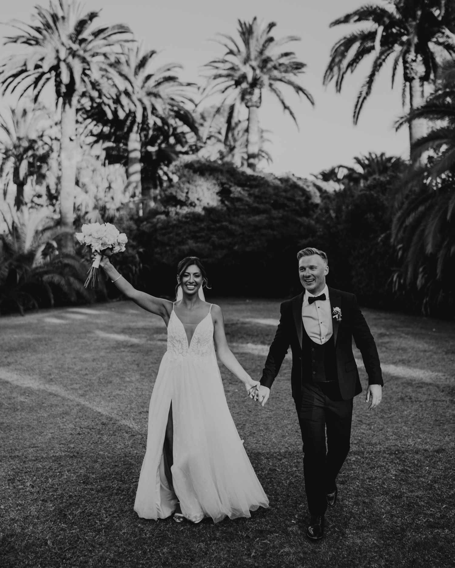 A black and white wedding photo of a couple celebrating under palm trees.