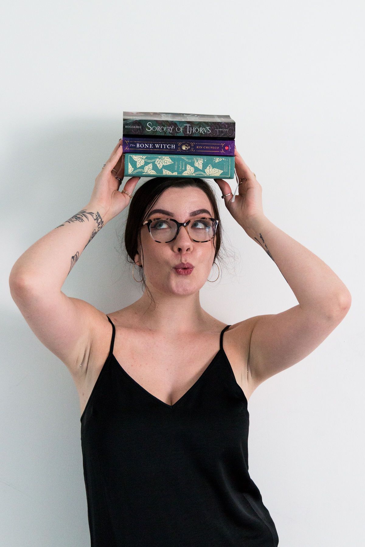 RVA Richmond Virginia senior photographer. Young woman in a black dress holding a stack of books on her head. Book nerd photoshoot.
