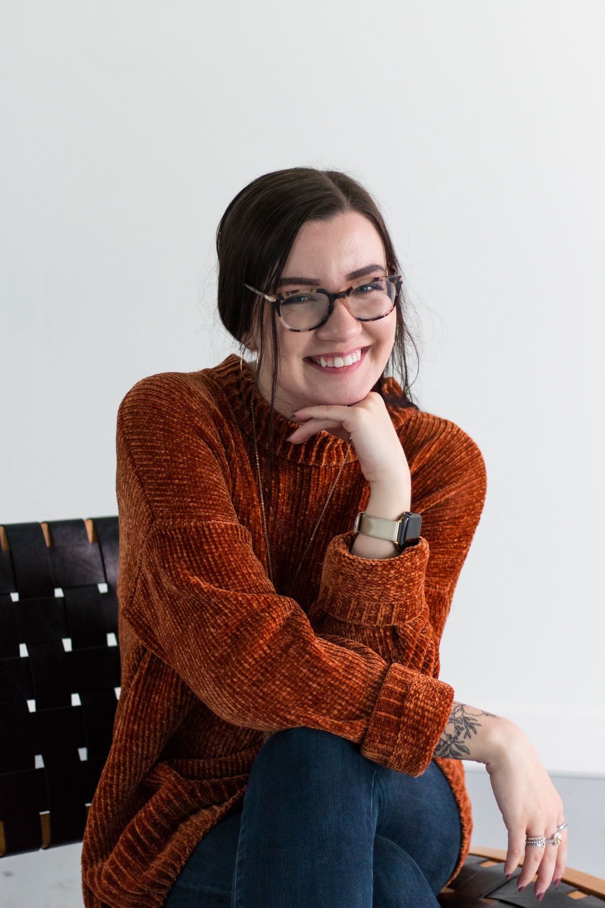 Young woman in an orange sweater and glasses smiling at the camera. RVA Richmond Virginia senior photographer.