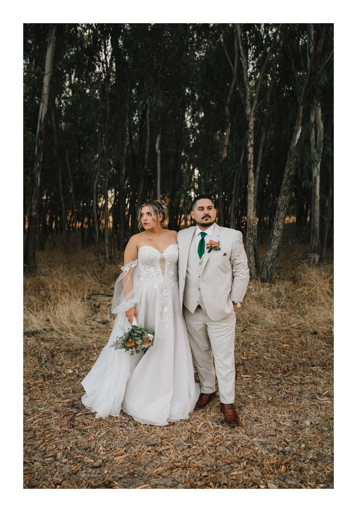 A romantic forest wedding photo featuring a couple in light colored formal attire among eucalyptus trees.