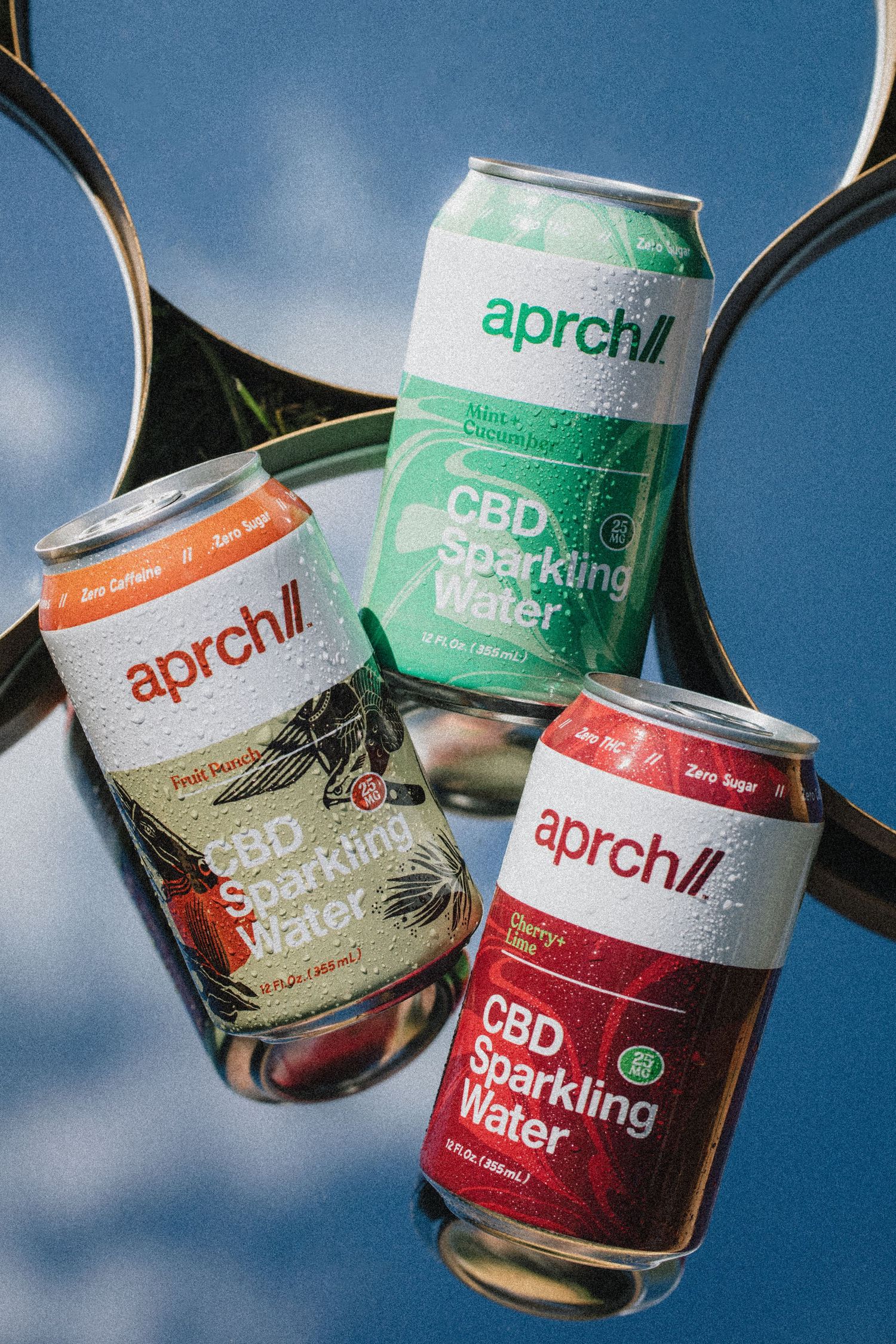 Three floating cans of Aprch CBD sparkling water in different flavors against a blue background with reflective surfaces.