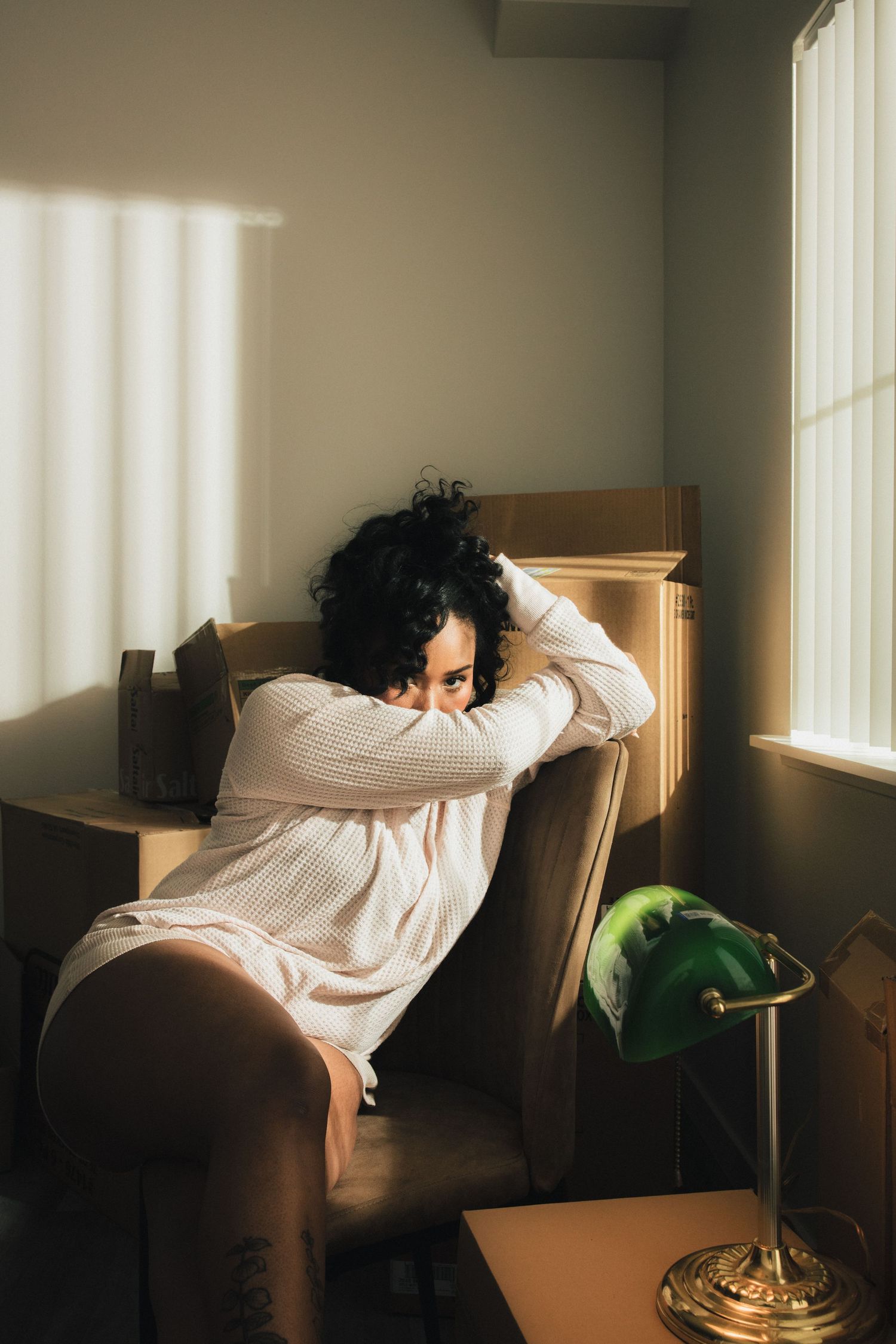 A person in white clothing reclines on a couch in a sunlit room with a green plant nearby.