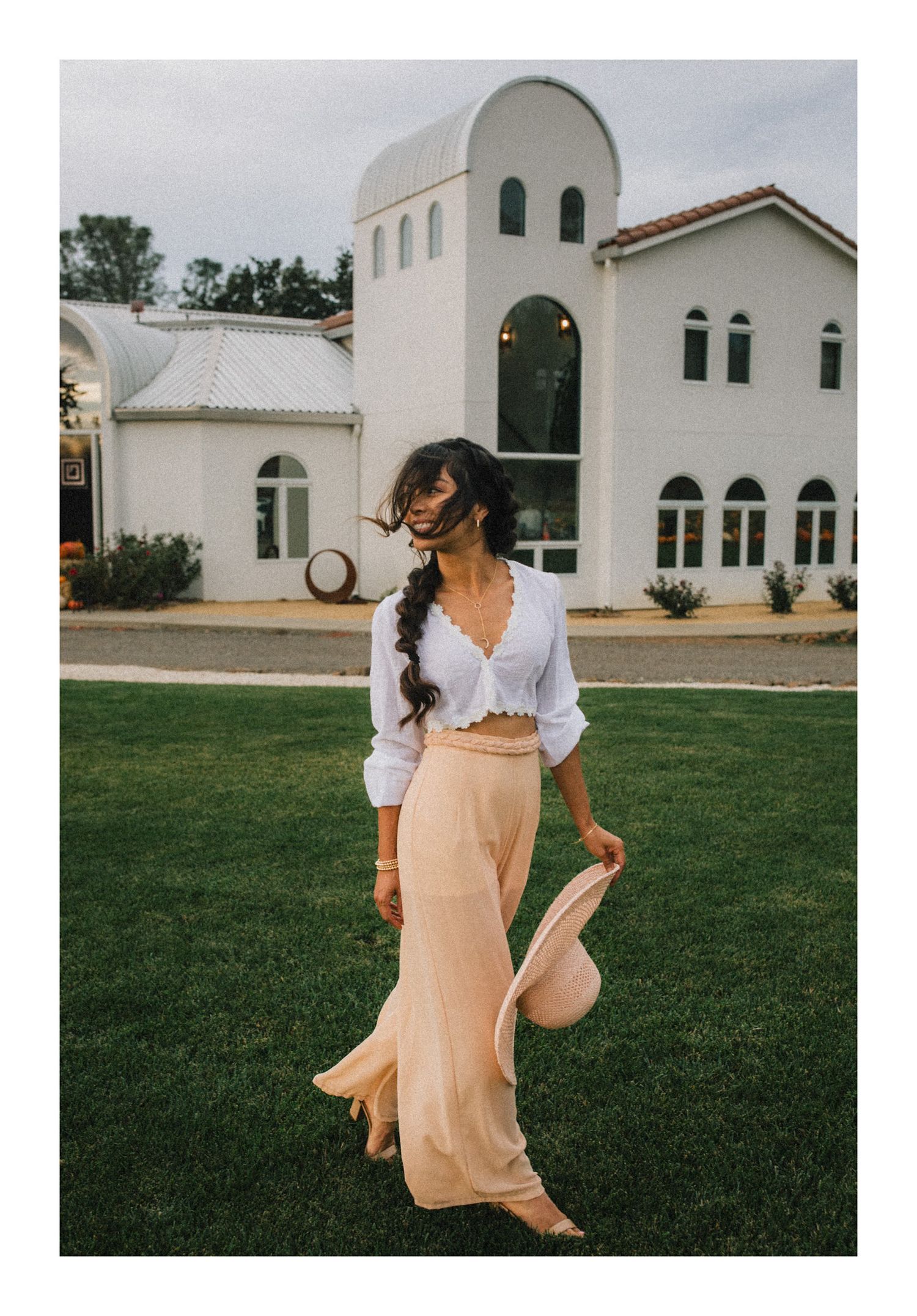 Woman in white crop top and flowing peach maxi skirt stands in front of Mediterranean-style white church building.
