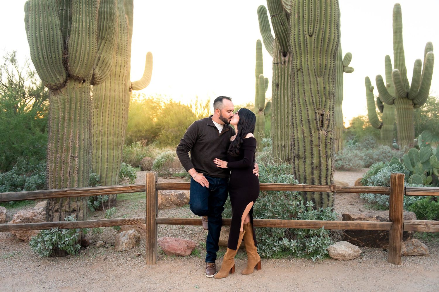 A couple shares a kiss in front of Saguaros in the Riparian Preserve cactus garden at golden hour during their Arizona family photo session.