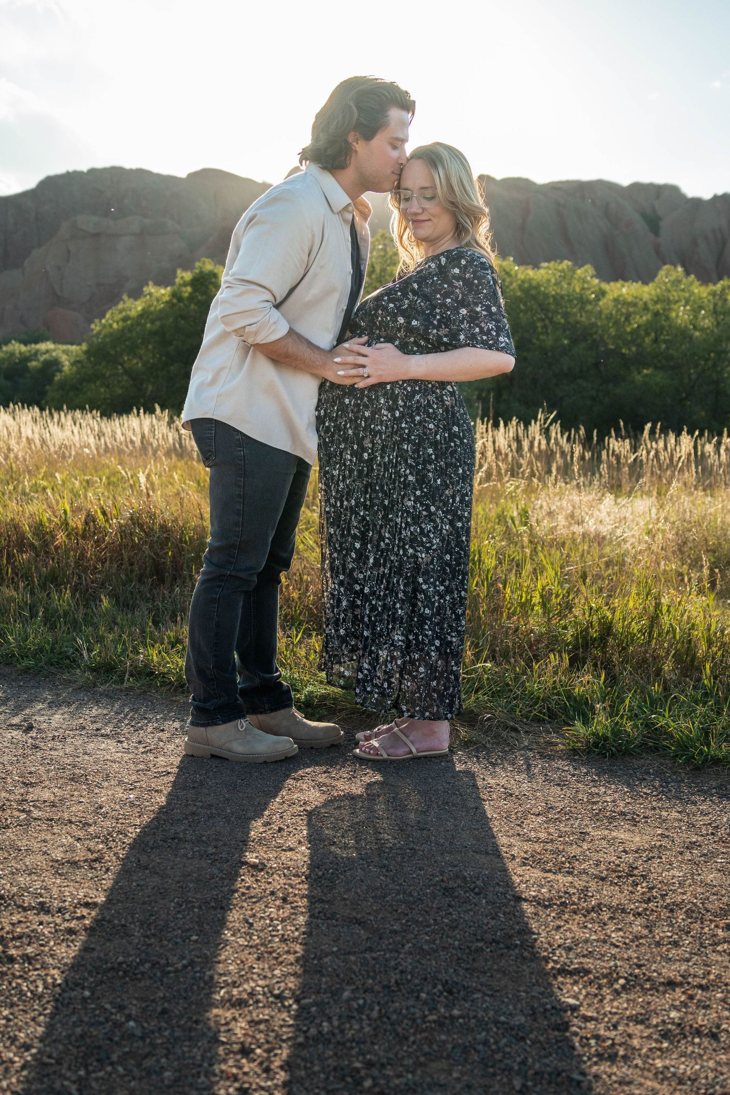 A couple embracing in golden sunlight with mountain cliffs and long shadows in the background.
