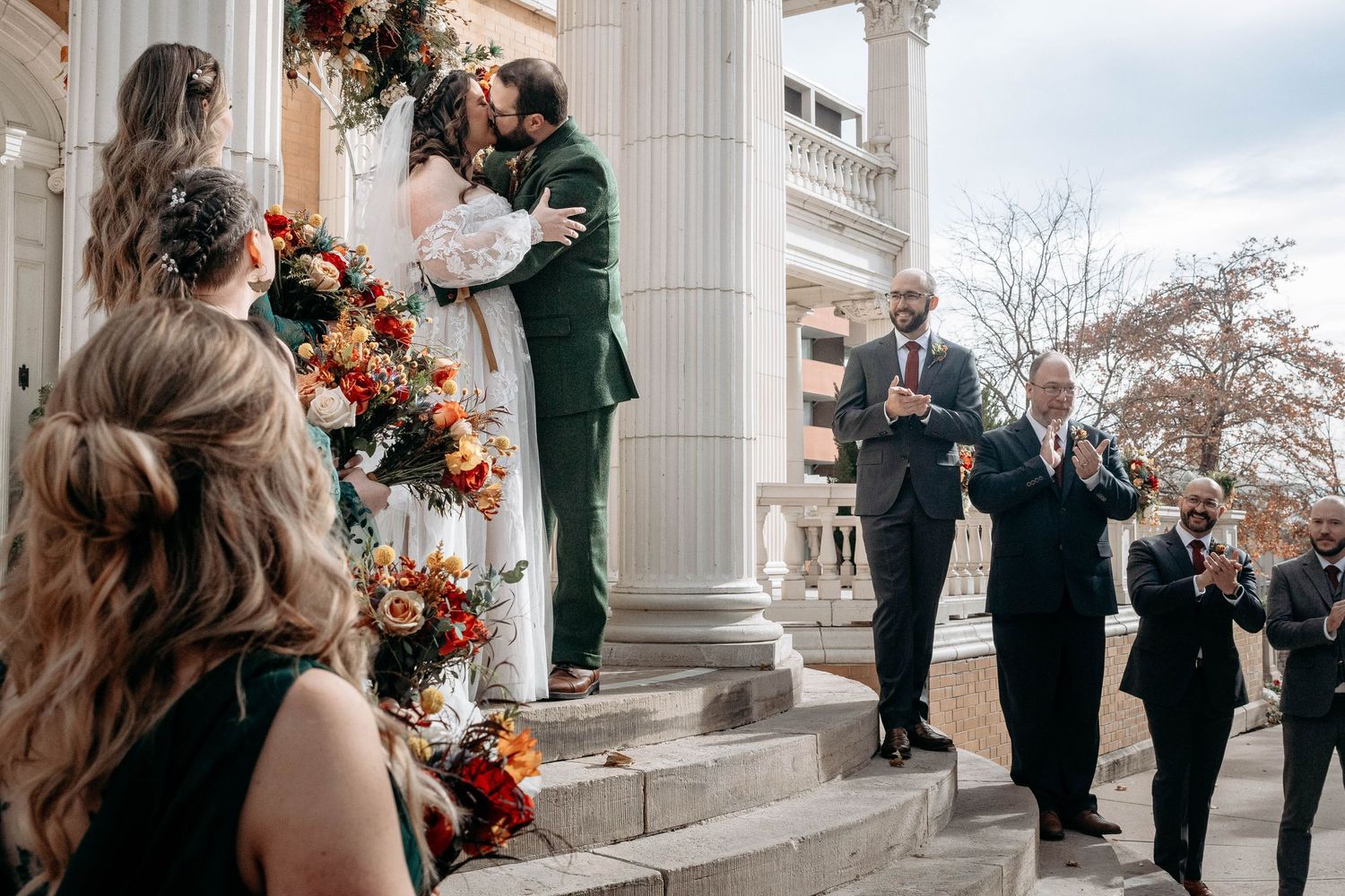 An outdoor autumn wedding ceremony with floral decorations on classical white columns.