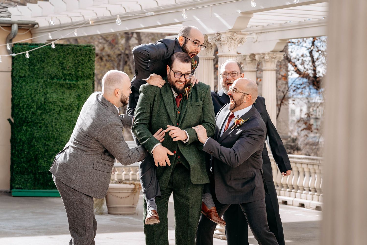 Groomsmen celebrating and jumping with joy at outdoor wedding venue.
