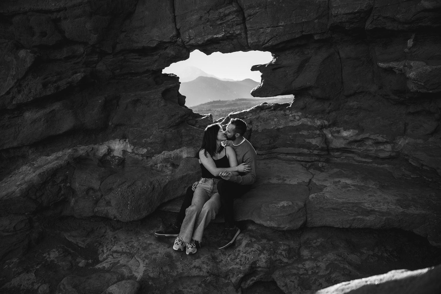 A tender moment captured in black and white as two people embrace within a rocky cave opening.