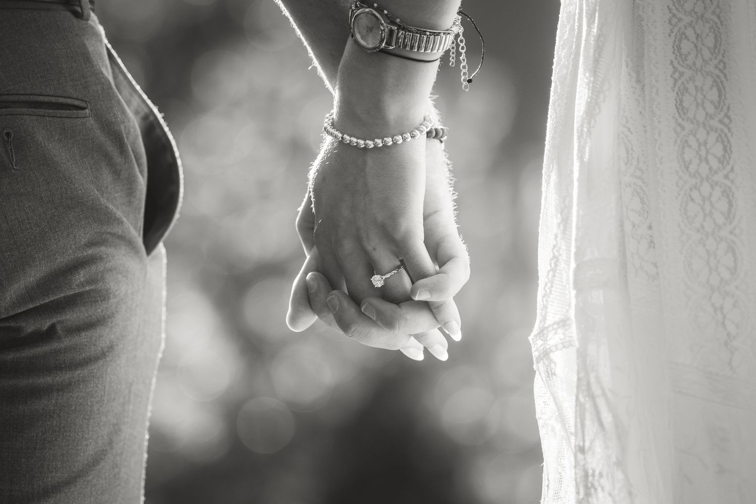 Black and white photo of a couple holding hands, bride wearing a pearl bracelet and engagement ring.