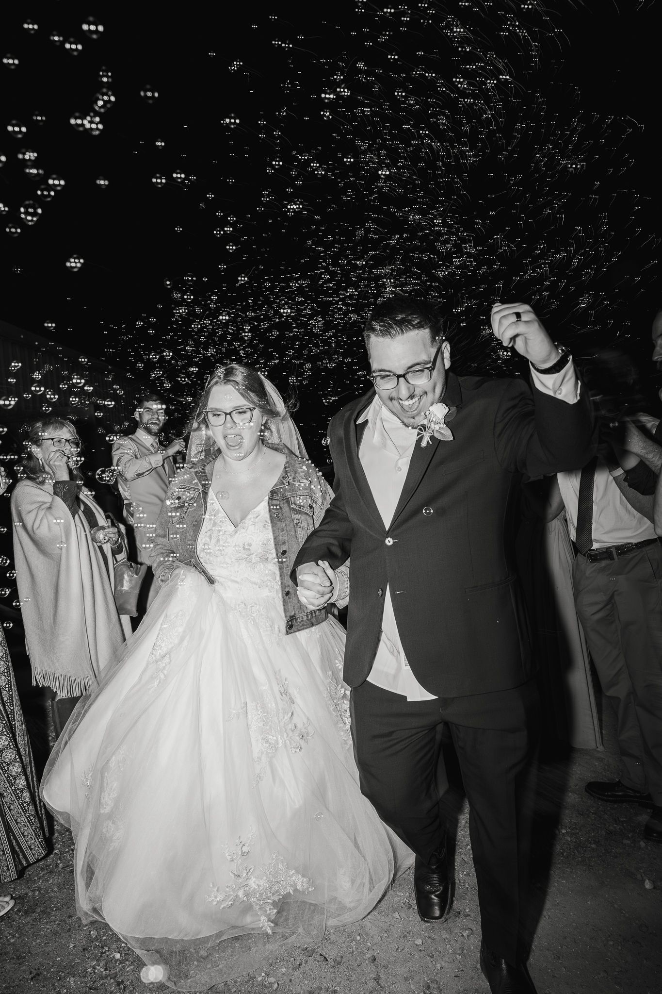 Black and white photo of a joyful bride and groom walking through a bubble send-off at their wedding reception.