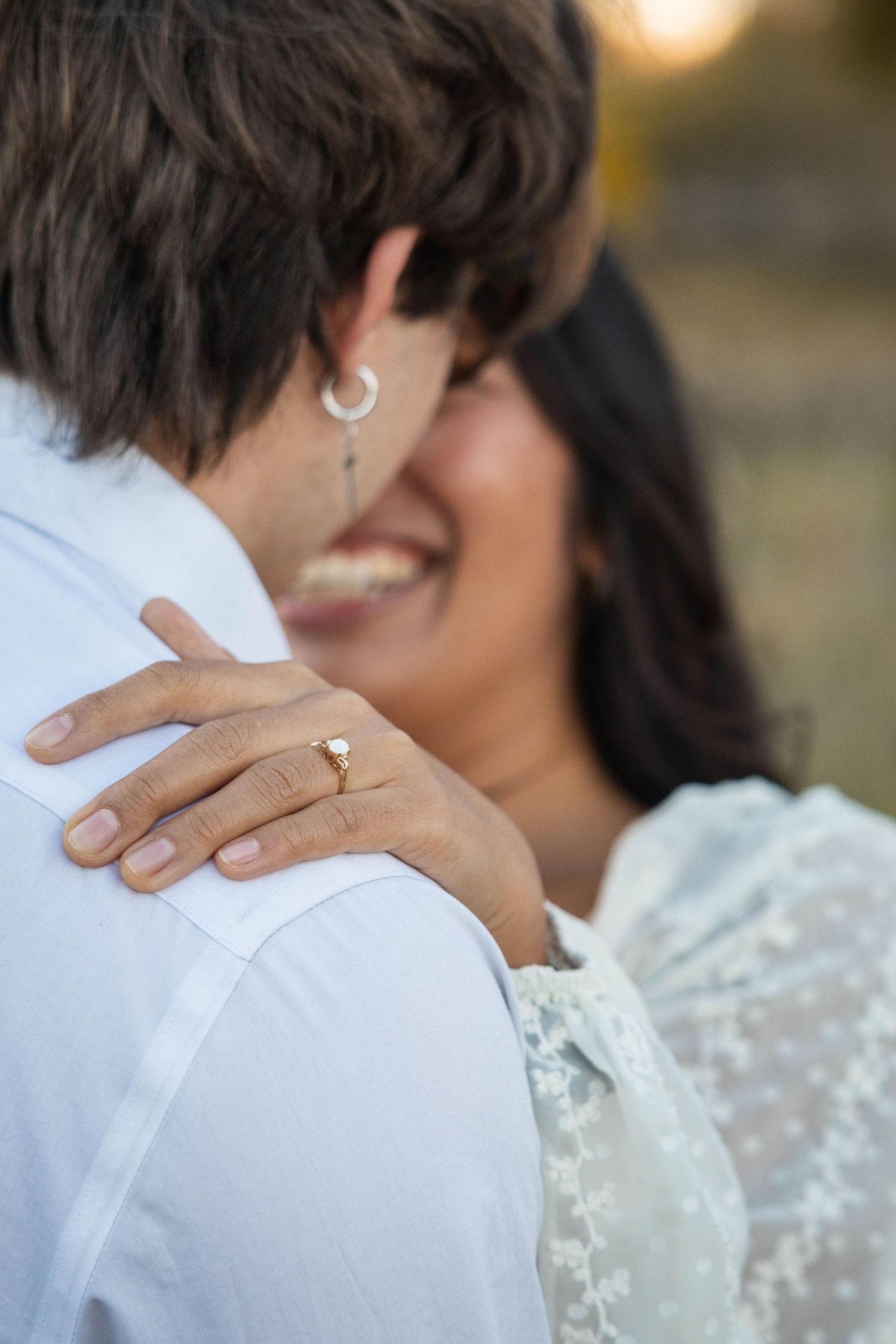 Close up of a couple embracing showing hands with rings and lace dress details in golden sunlight.