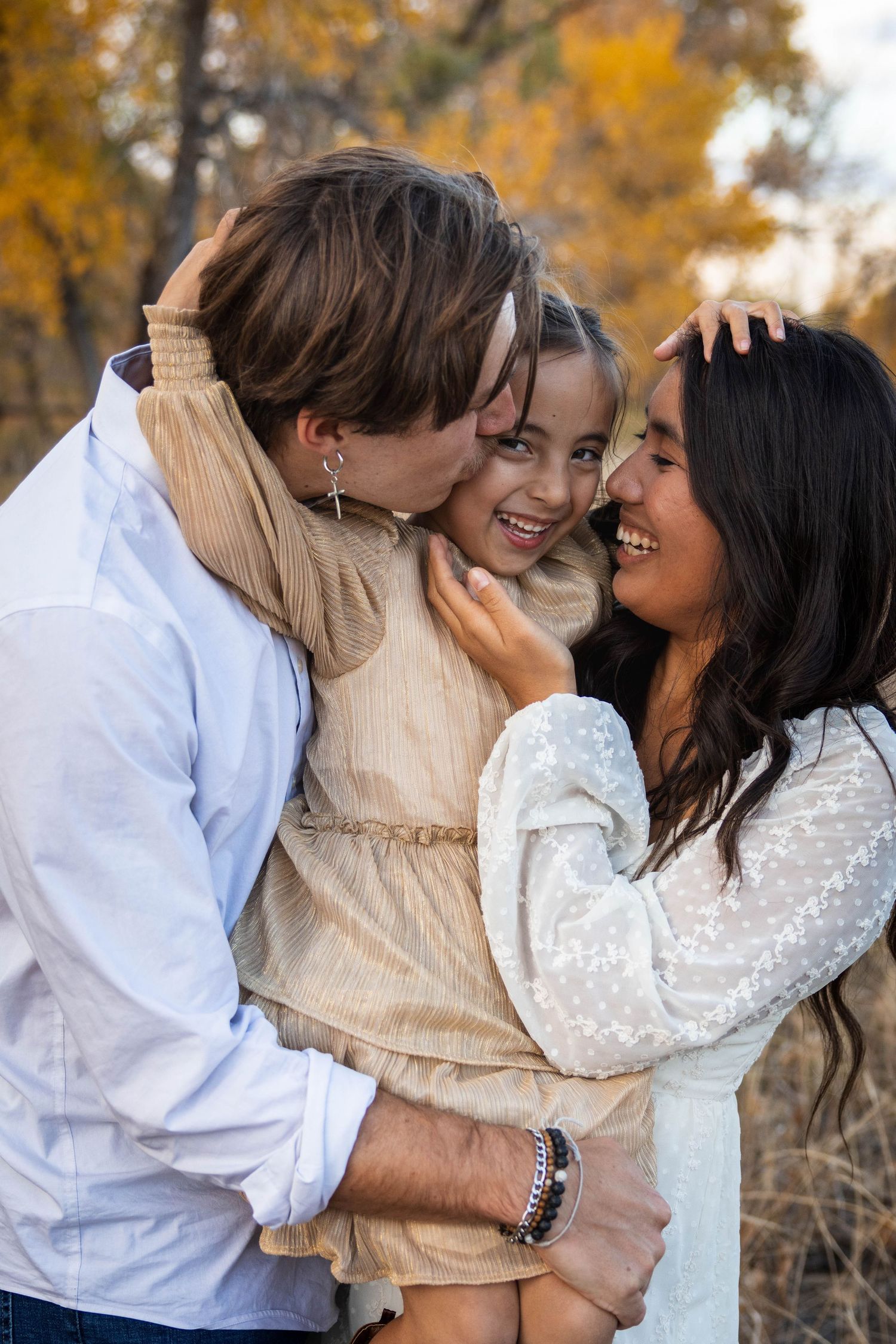 Family sharing intimate moment outdoors with autumn foliage in background.