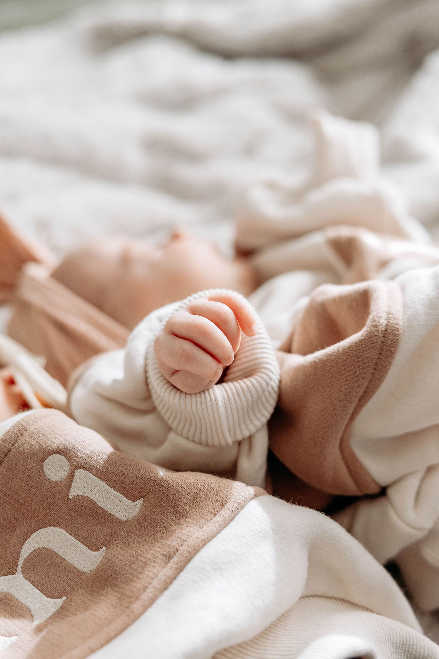 Close up of beige and white knitted baby clothing arranged in a soft, delicate pattern.