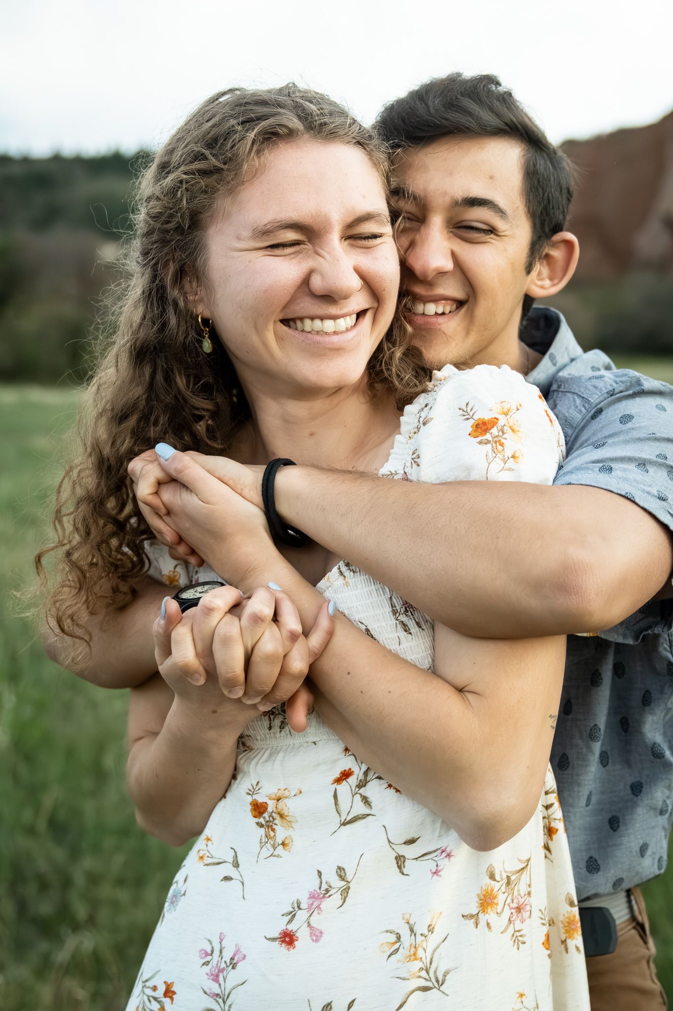 Happy young couple embracing outdoors, laughing joyfully in a green field setting.